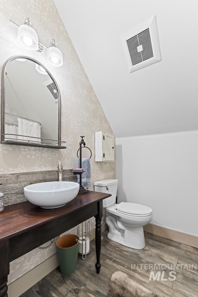 Bathroom featuring dark wood-type flooring, wallpapered walls, and vaulted ceiling