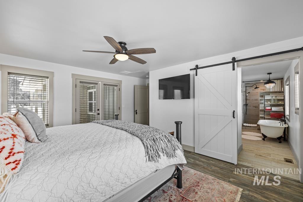 Bedroom with dark wood-style flooring, ceiling fan, and a barn door