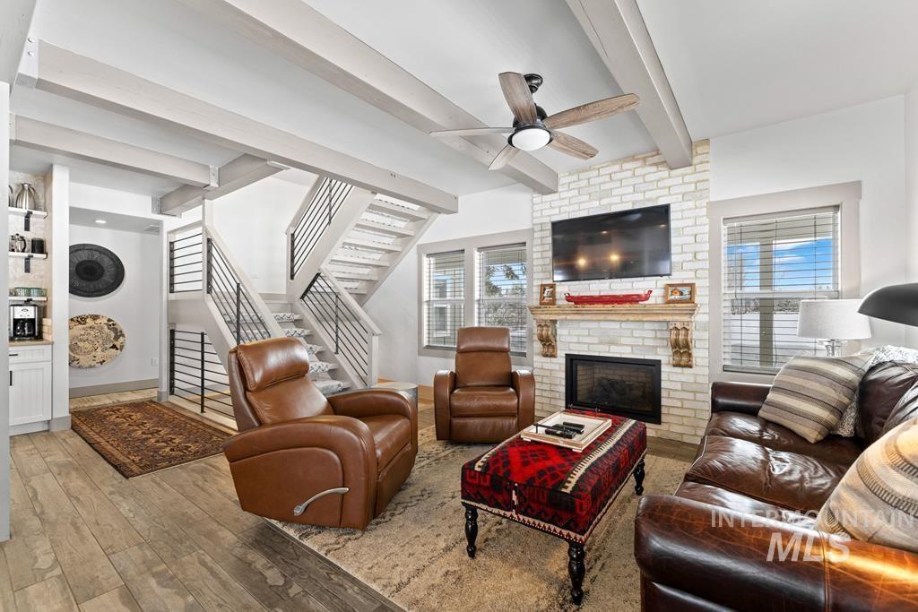 Living room with beamed ceiling, stairs, light wood-type flooring, a brick fireplace, and ceiling fan