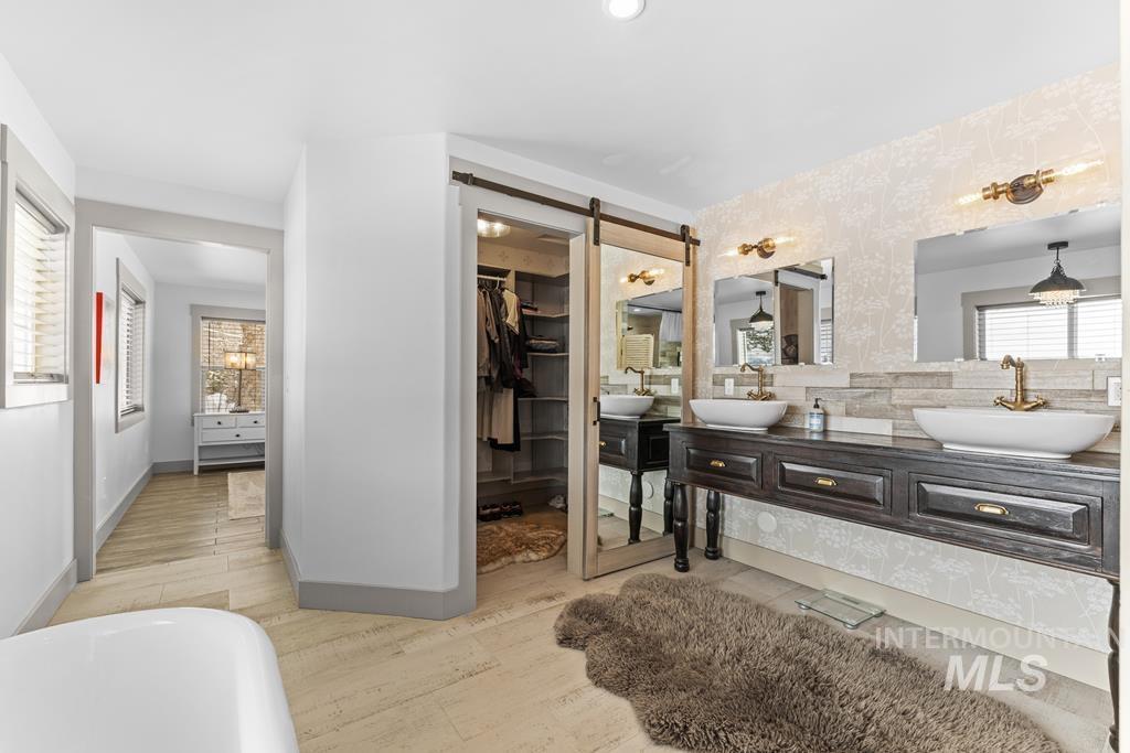 Full bathroom featuring double vanity, a soaking tub, light wood finished floors, and a spacious closet