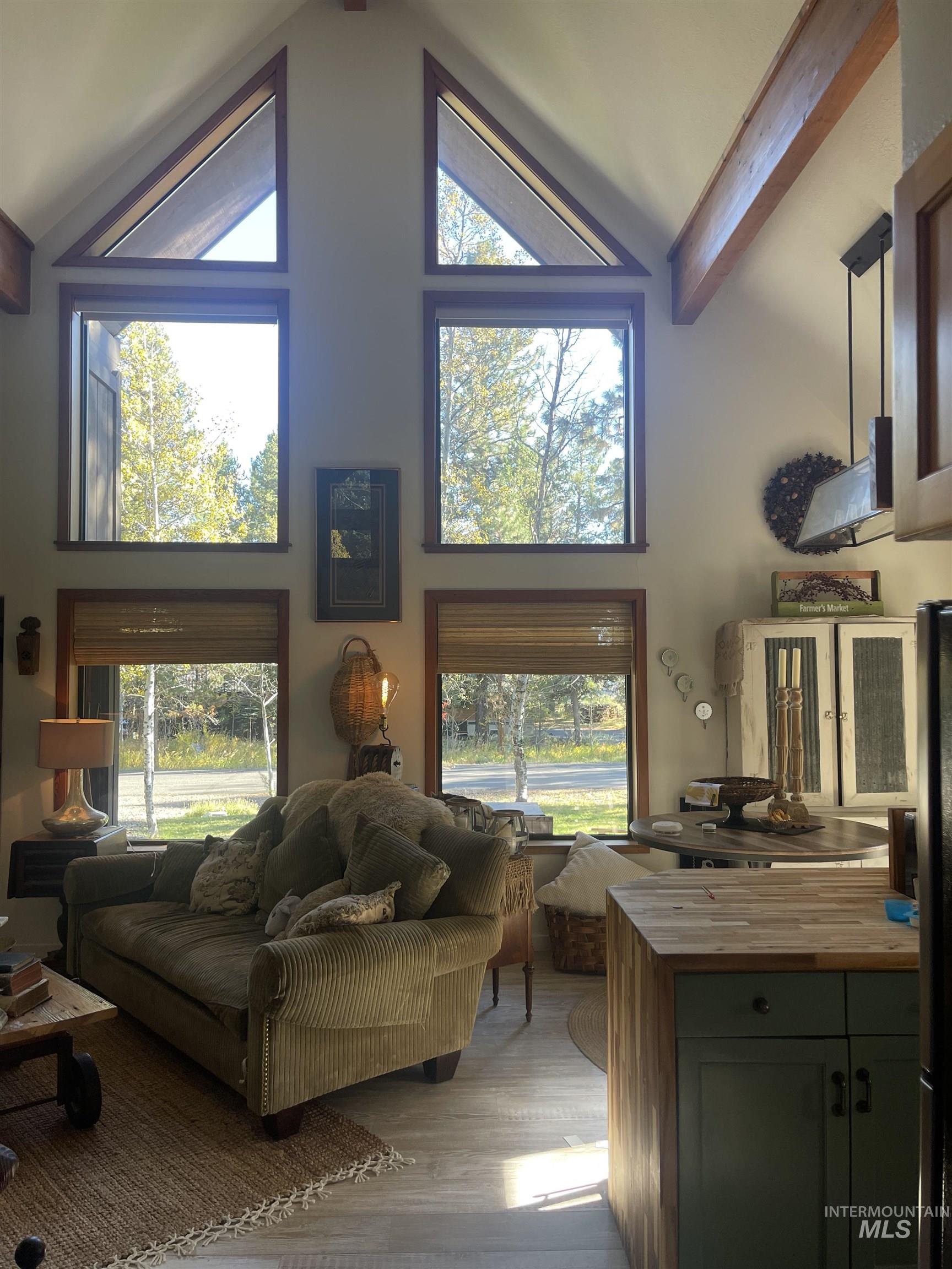 Living room with high vaulted ceiling, wood finished floors, beam ceiling, and plenty of natural light