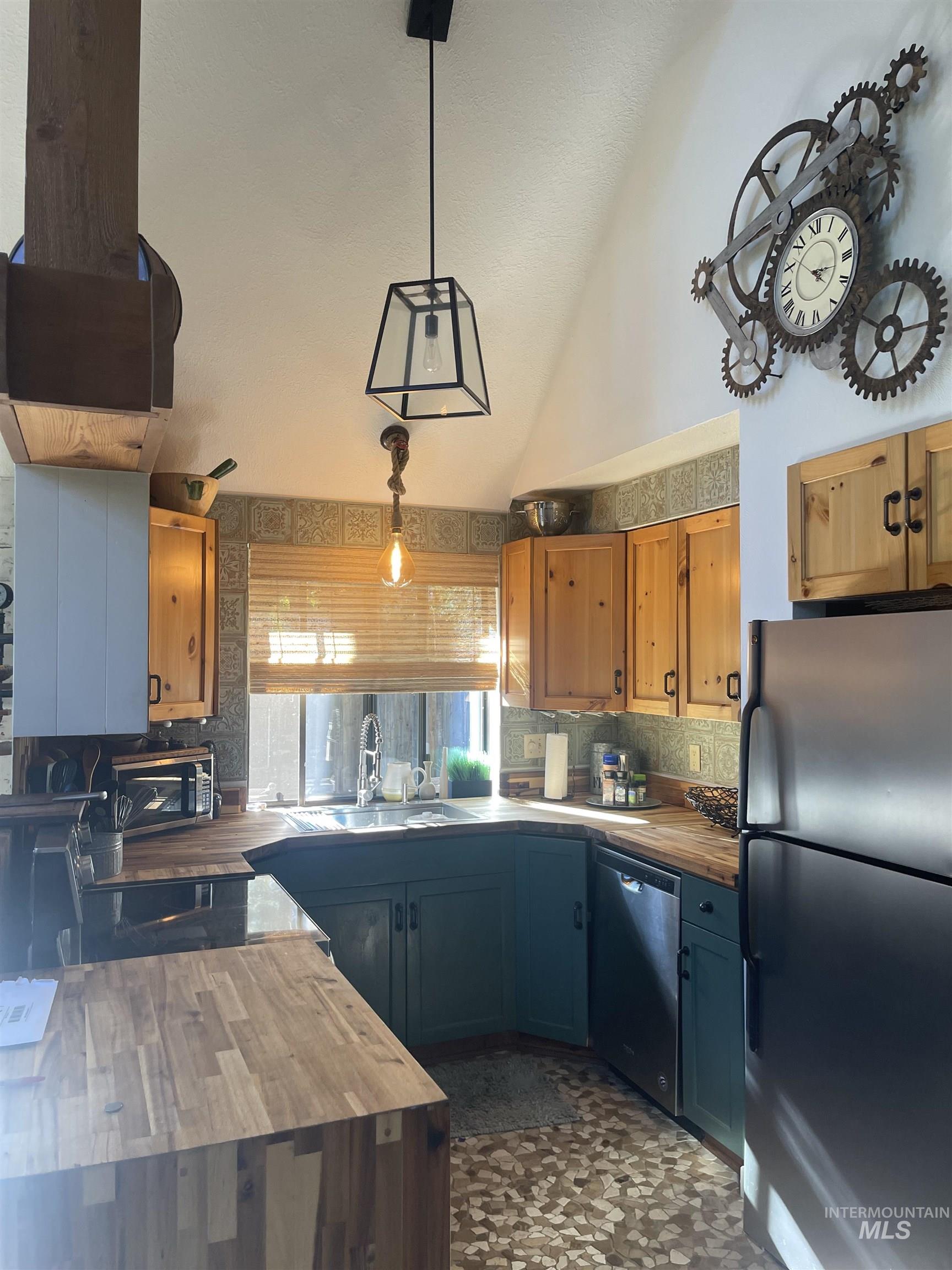 Kitchen with appliances with stainless steel finishes, wooden counters, backsplash, lofted ceiling, and decorative light fixtures
