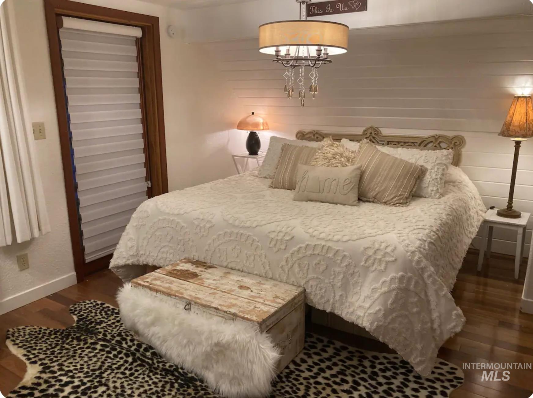 Bedroom with dark wood-style flooring, wooden walls, and a chandelier