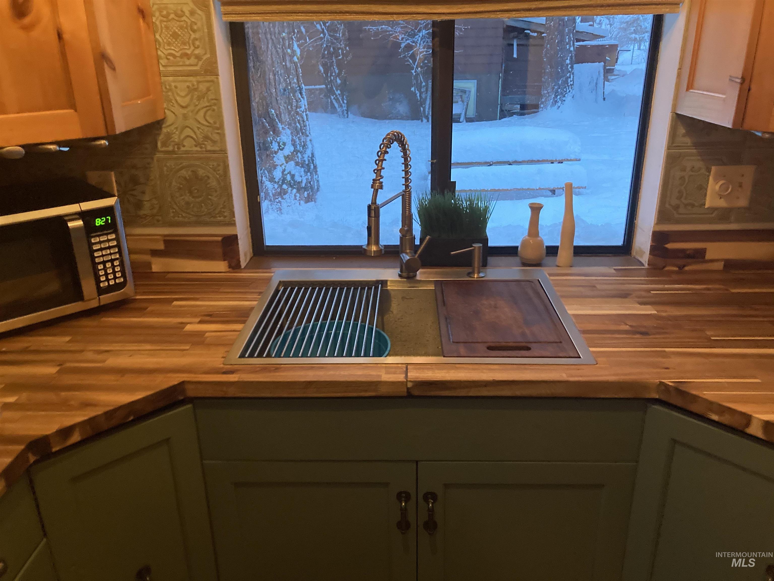 Kitchen with green cabinets, stainless steel microwave, butcher block countertops, and wallpapered walls