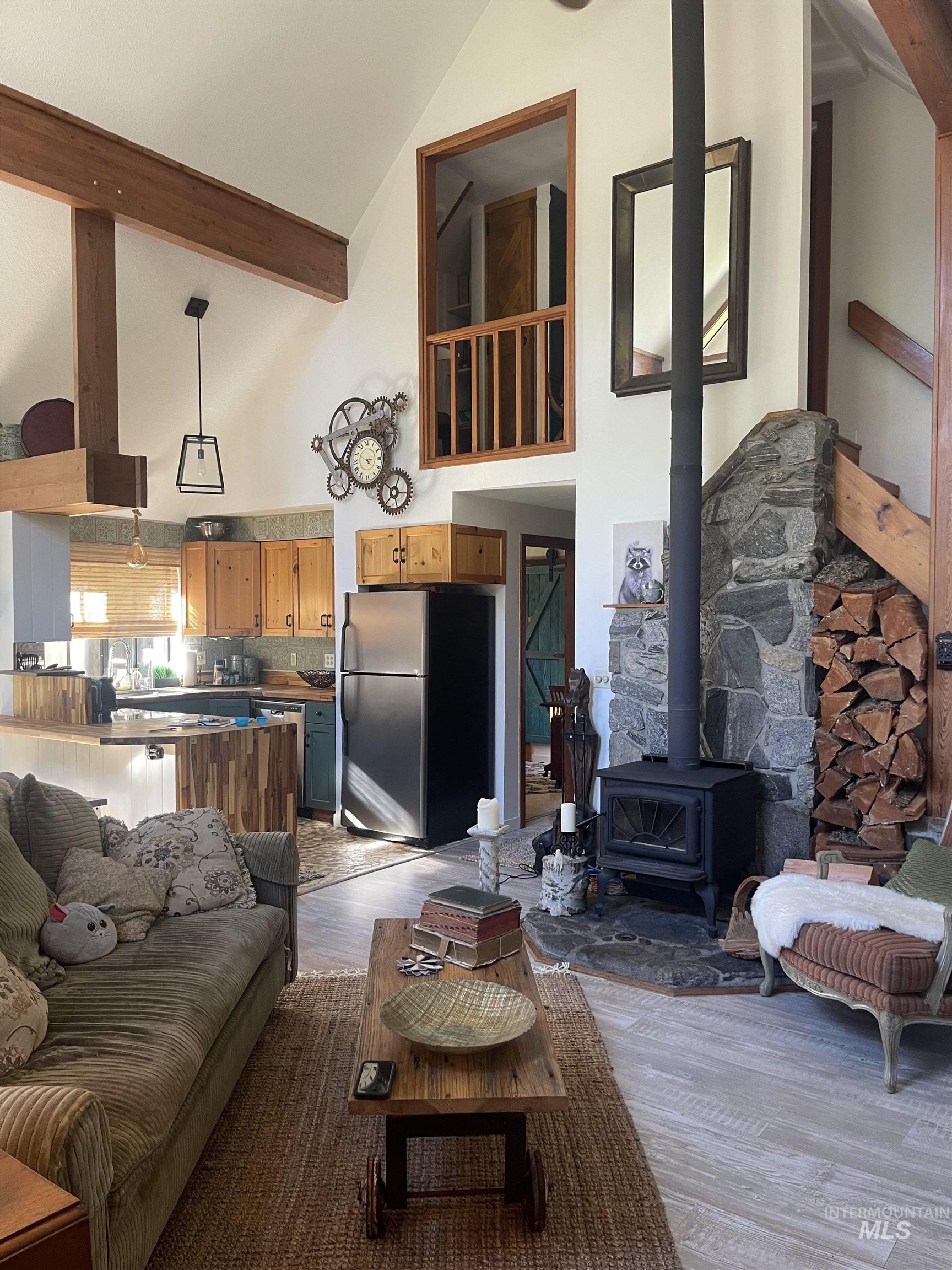 Living room featuring a wood stove, high vaulted ceiling, light wood finished floors, and beamed ceiling