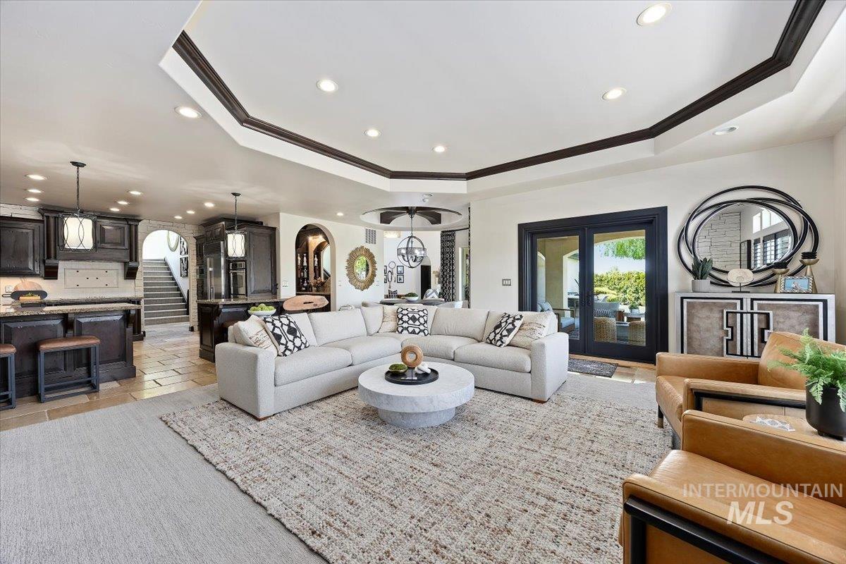 Living area with a raised ceiling, crown molding, recessed lighting, stairs, and arched walkways