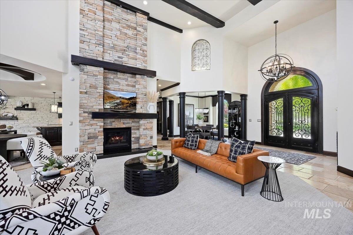 Living area with a fireplace, a chandelier, beam ceiling, a towering ceiling, and french doors