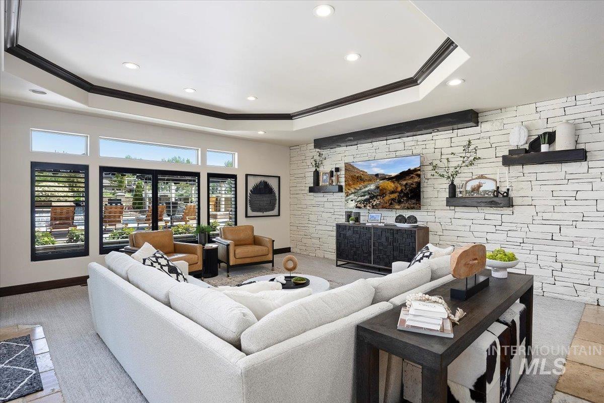 Living room featuring a raised ceiling, crown molding, an accent wall, and recessed lighting