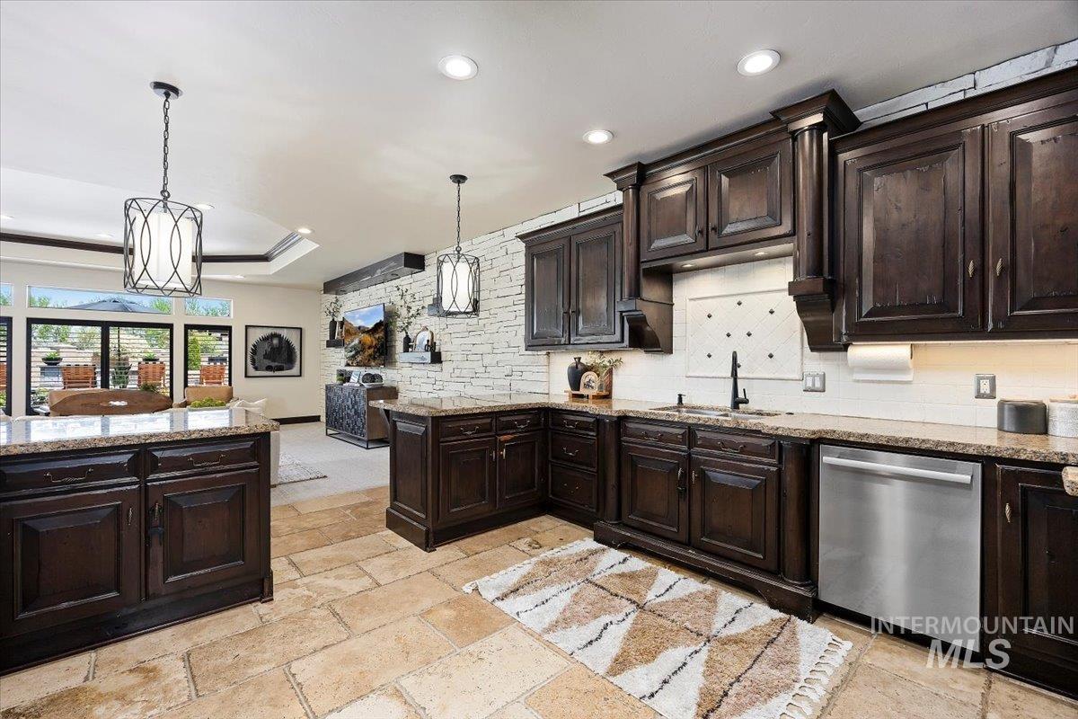 Kitchen featuring dishwasher, backsplash, decorative light fixtures, stone tile flooring, and dark brown cabinetry