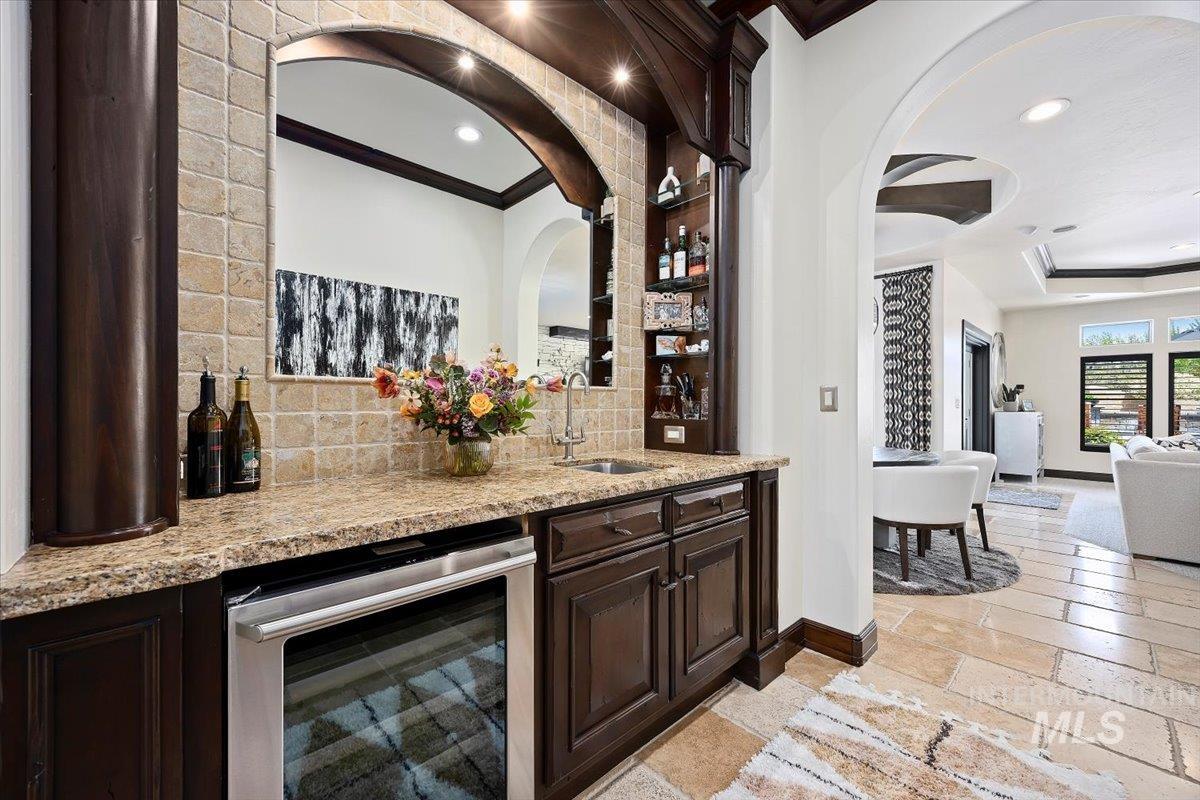 Indoor bar featuring beverage cooler, recessed lighting, stone tile flooring, arched walkways, and decorative backsplash
