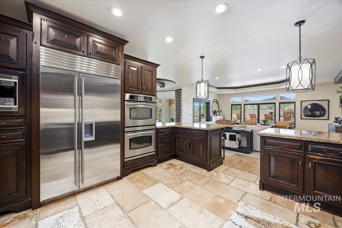 Kitchen with built in appliances, recessed lighting, stone tile flooring, dark brown cabinetry, and light stone counters