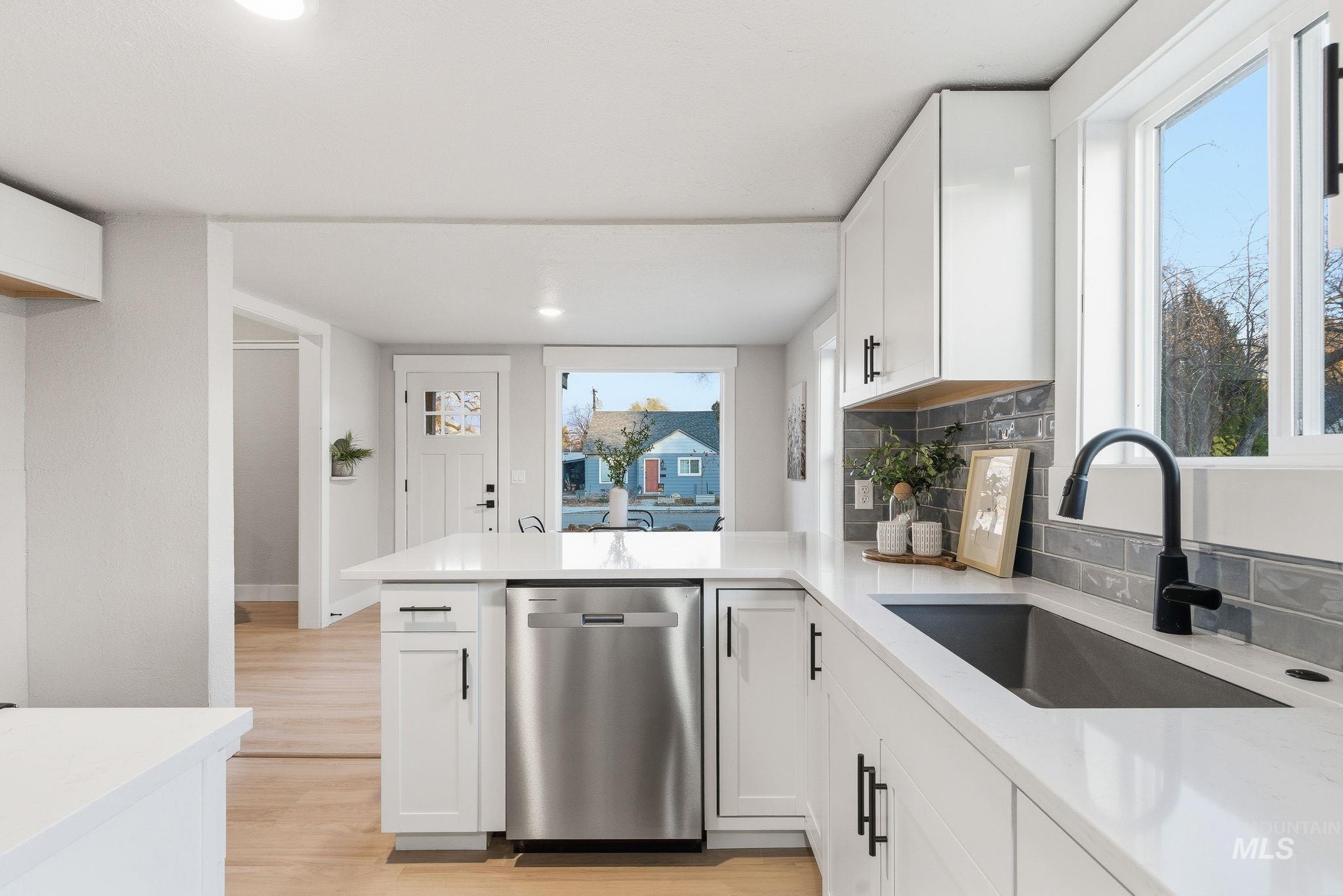 Kitchen with decorative backsplash, white cabinetry, dishwasher, a peninsula, and light wood-type flooring