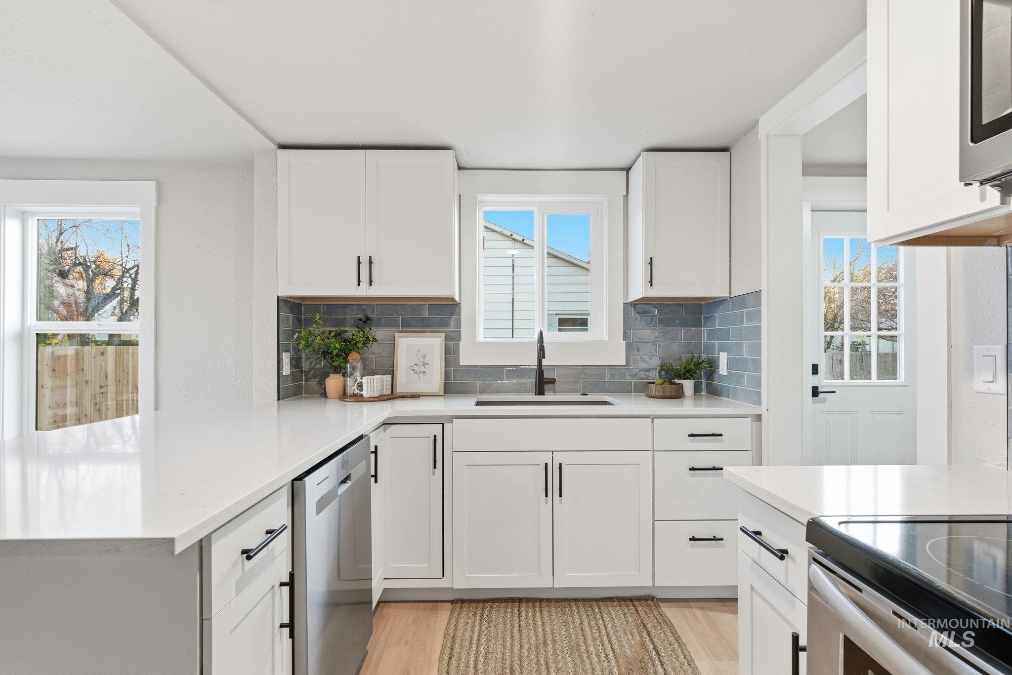 Kitchen with light wood-style floors, decorative backsplash, white cabinetry, a peninsula, and stainless steel appliances