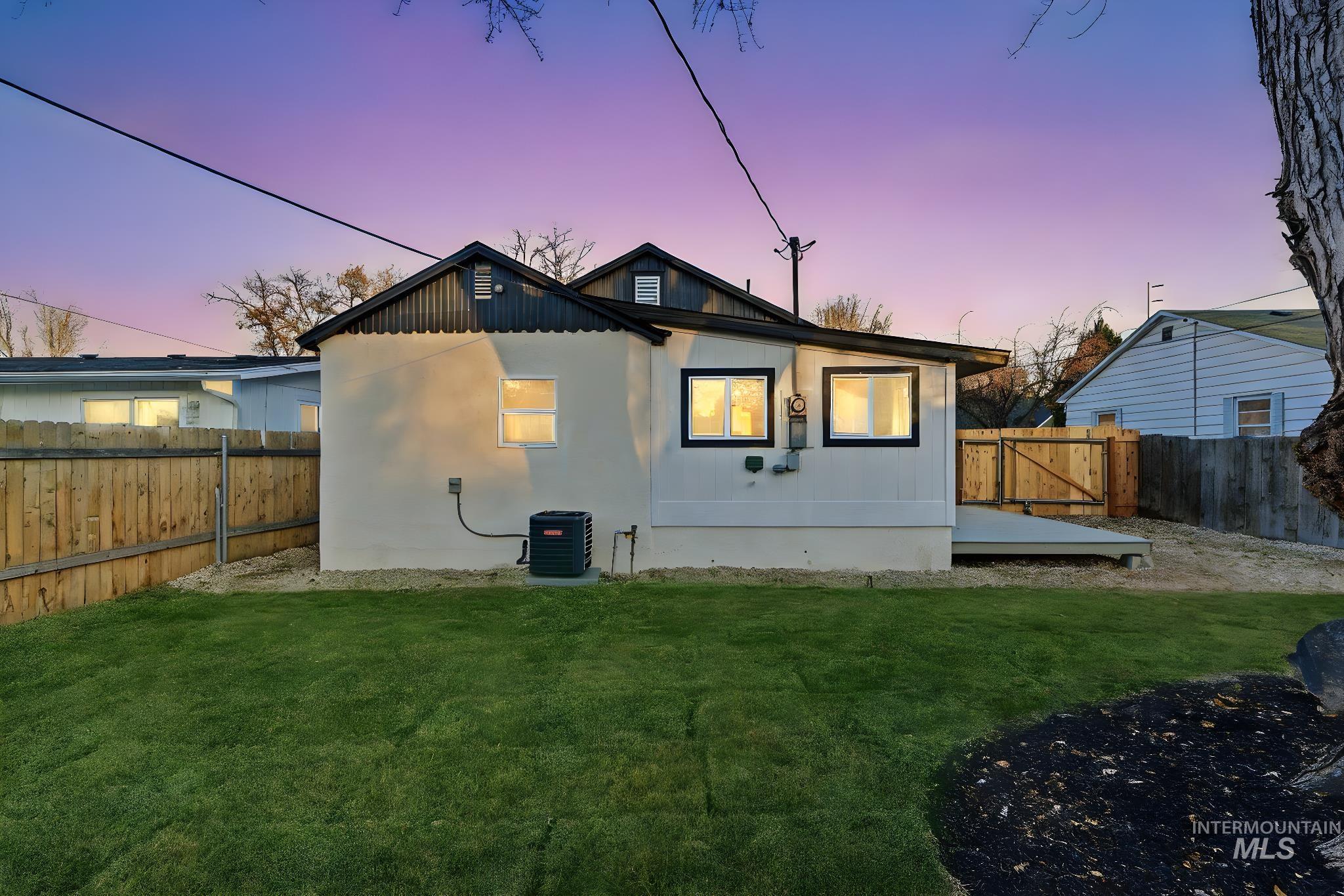 Back of property at dusk with a fenced backyard and a deck