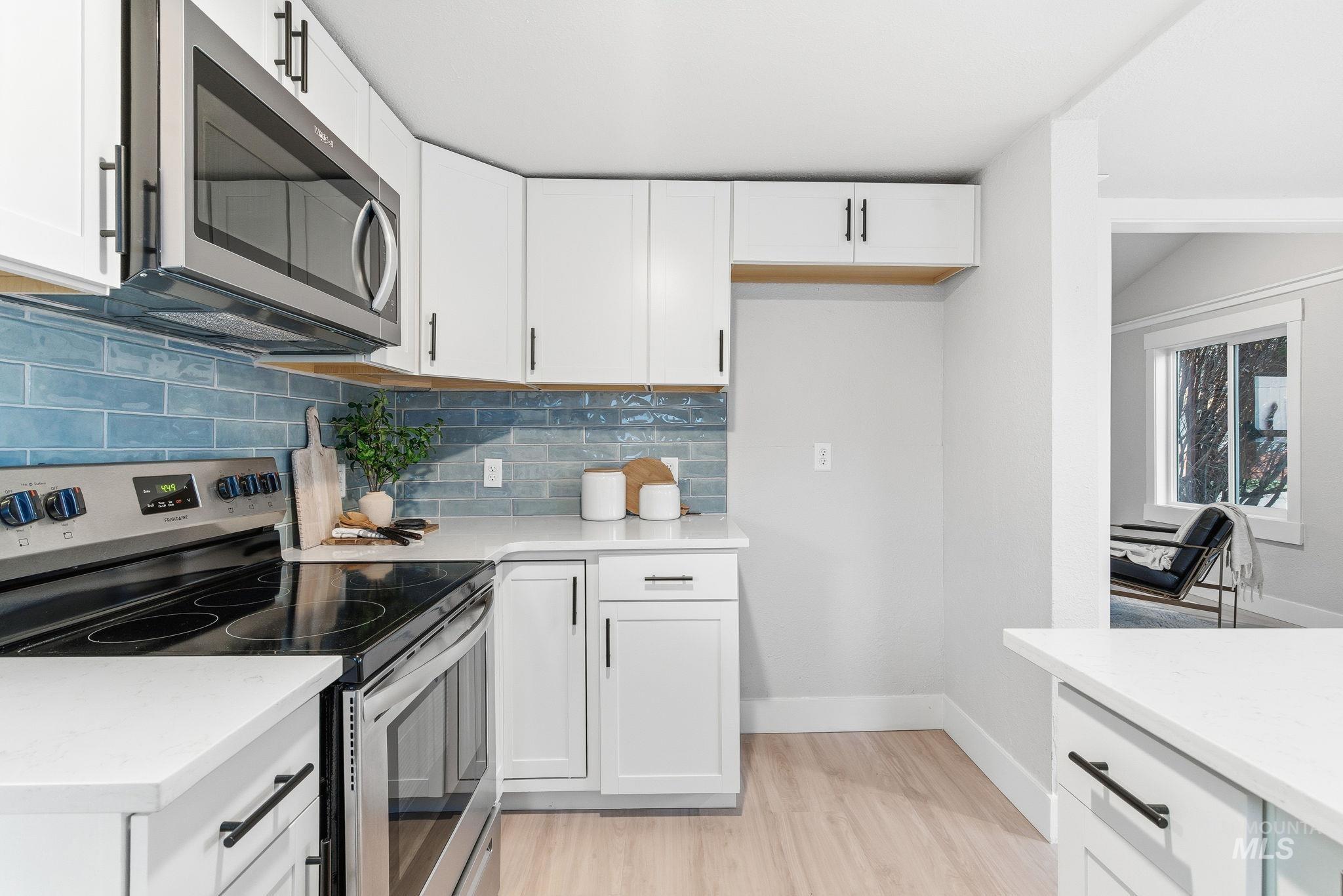 Kitchen with stainless steel appliances, white cabinetry, tasteful backsplash, and light wood-style flooring