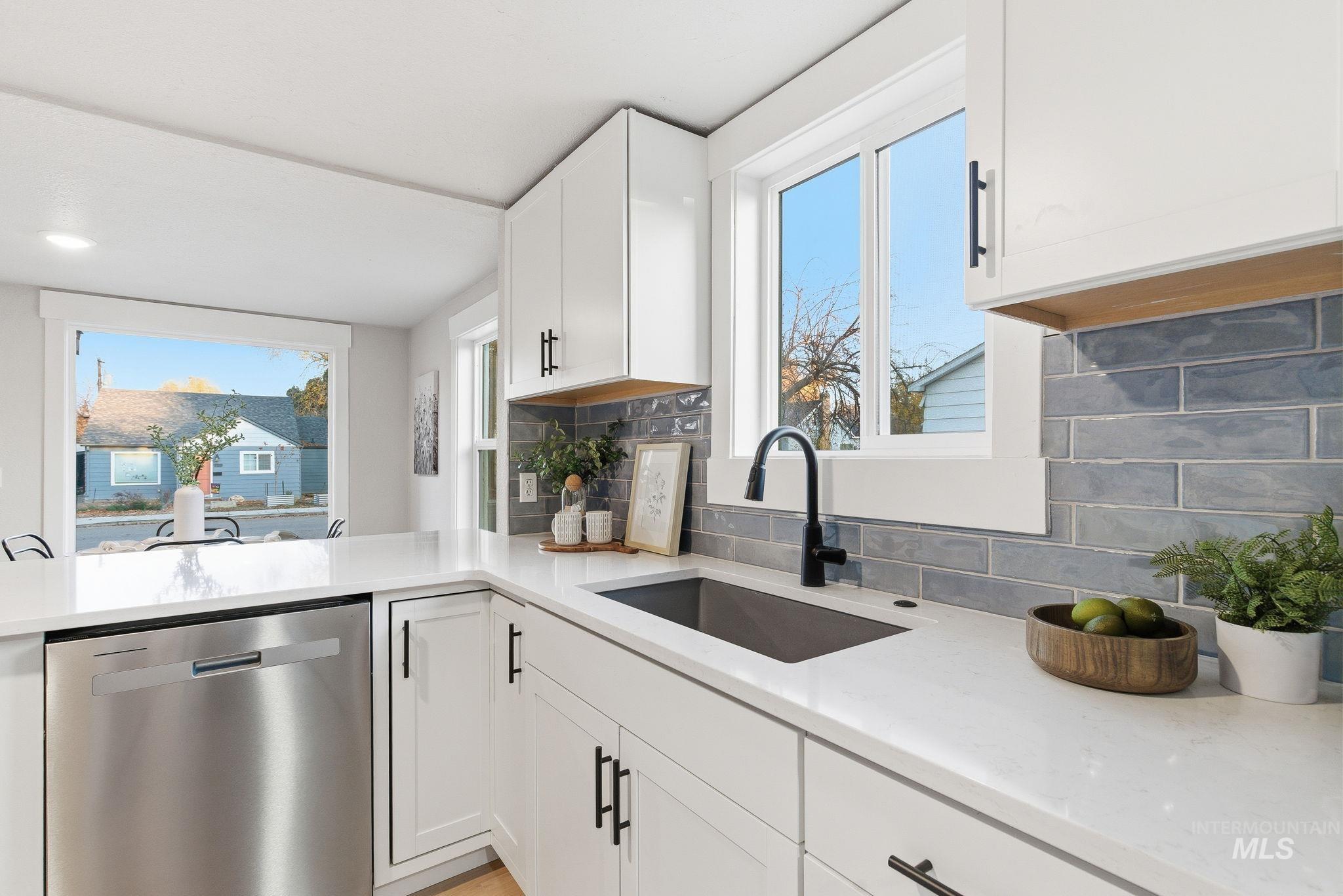 Kitchen with decorative backsplash, dishwasher, light stone counters, and white cabinetry