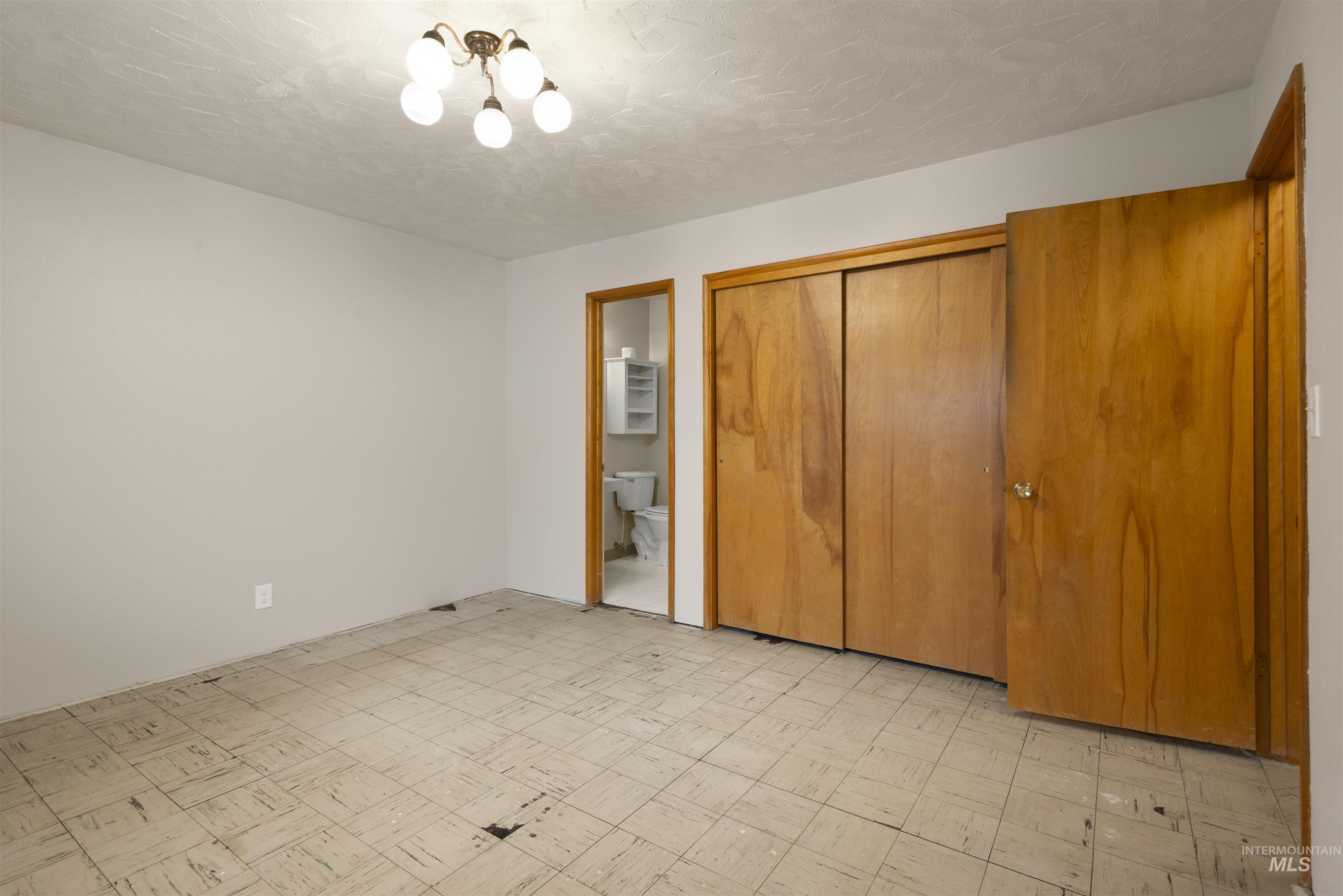 Unfurnished bedroom featuring a closet, light floors, connected bathroom, and a textured ceiling