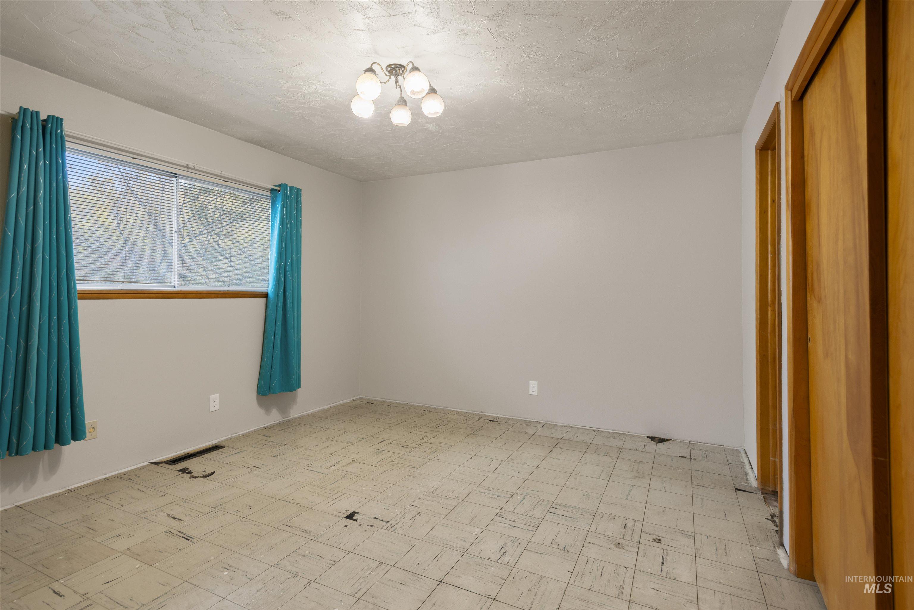 Spare room featuring light flooring, a textured ceiling, and a chandelier