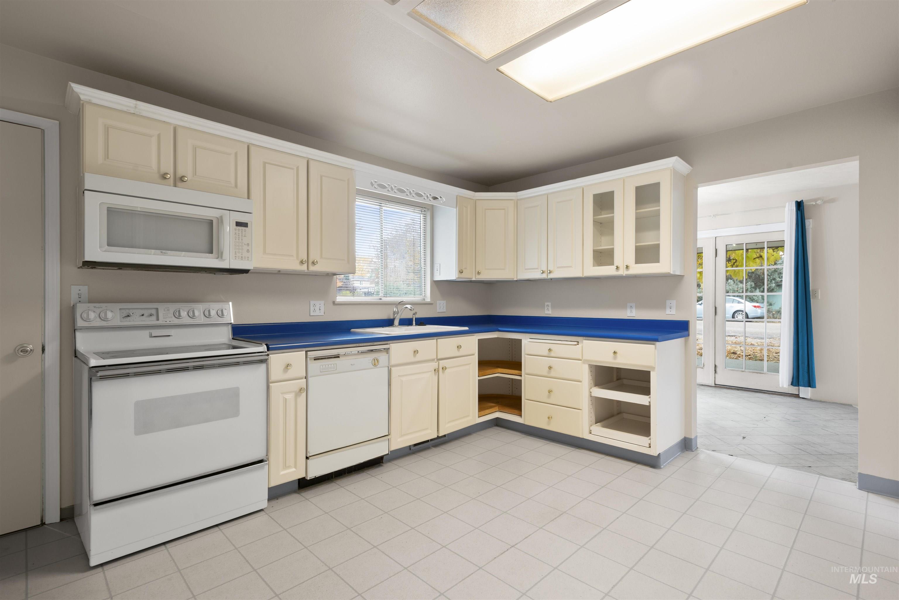Kitchen with white appliances, glass insert cabinets, light tile patterned flooring, and dark countertops