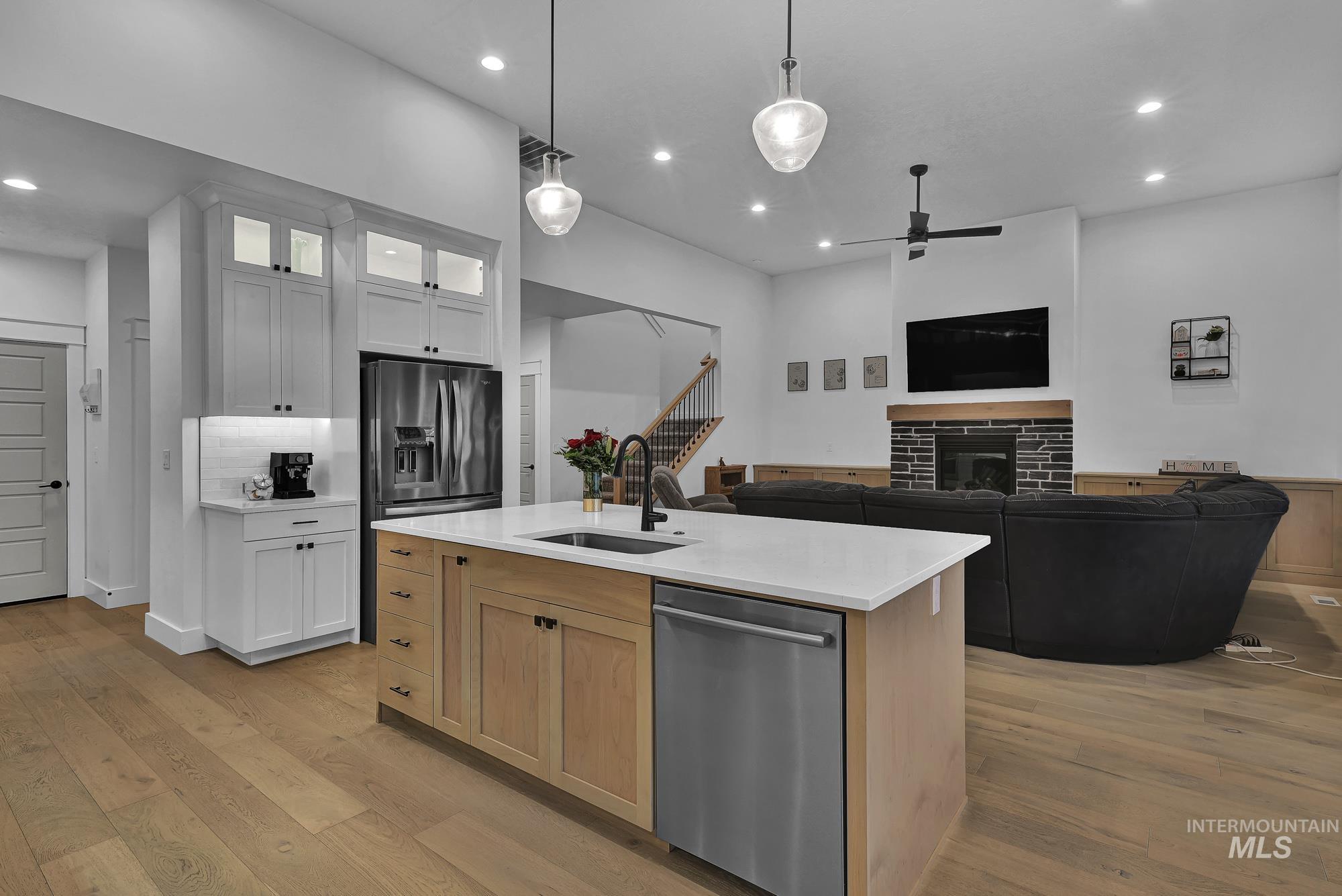 Kitchen with light brown cabinetry, light wood-type flooring, dishwasher, a center island with sink, and open floor plan