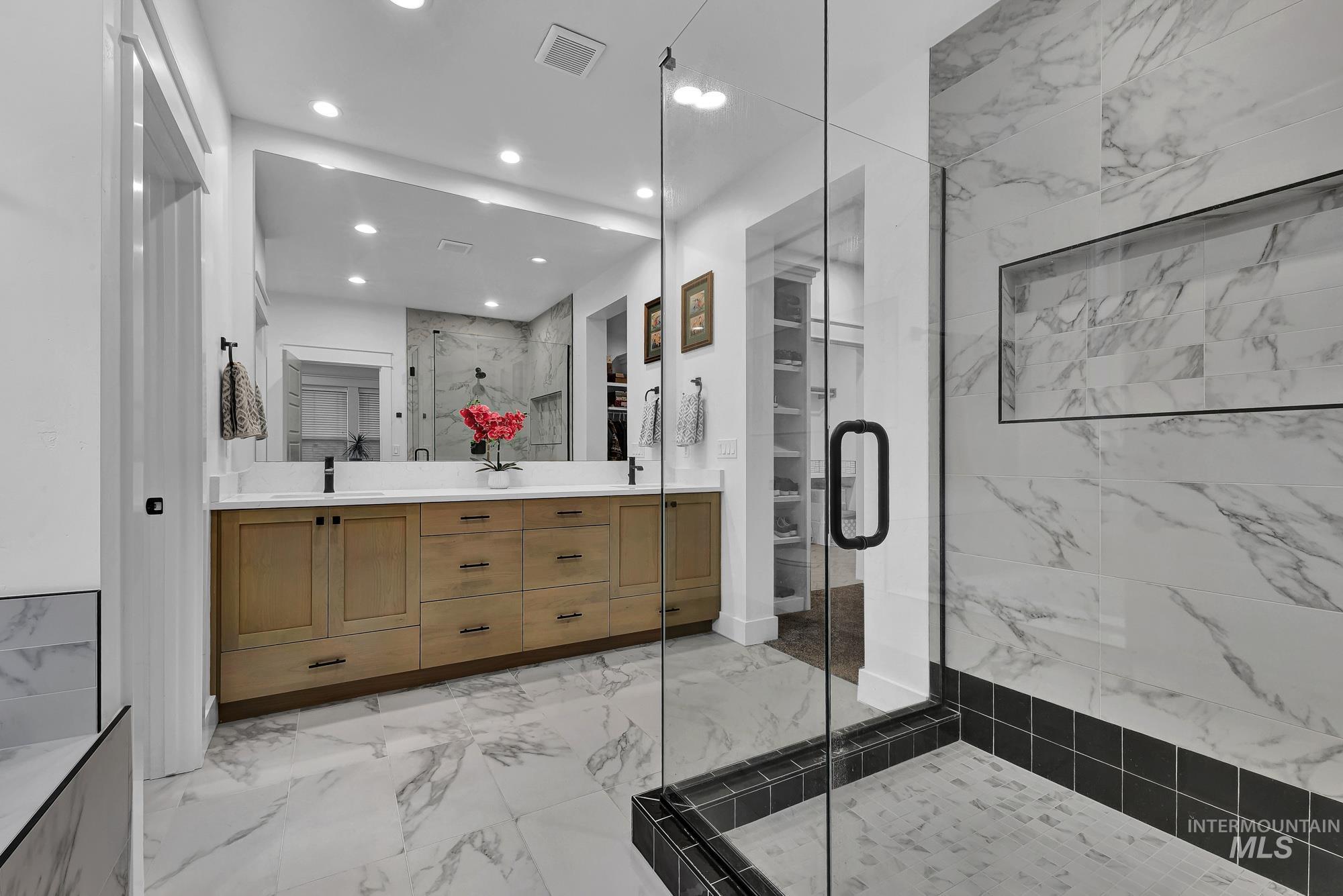Bathroom featuring double vanity, a marble finish shower, light marble finish flooring, and recessed lighting