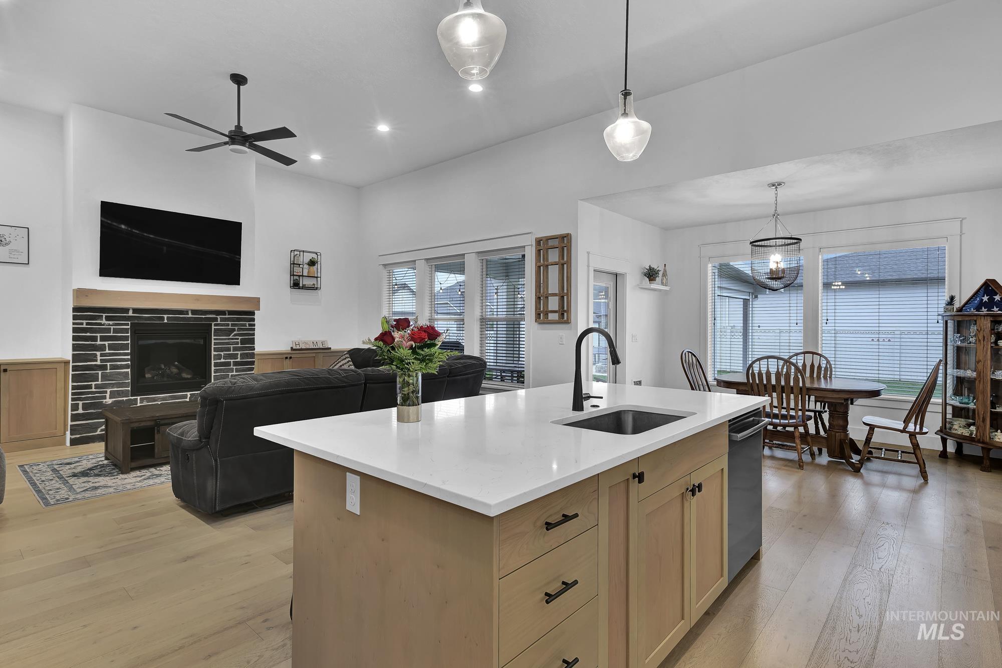Kitchen featuring light wood-style floors, light brown cabinetry, hanging light fixtures, a tiled fireplace, and light stone countertops