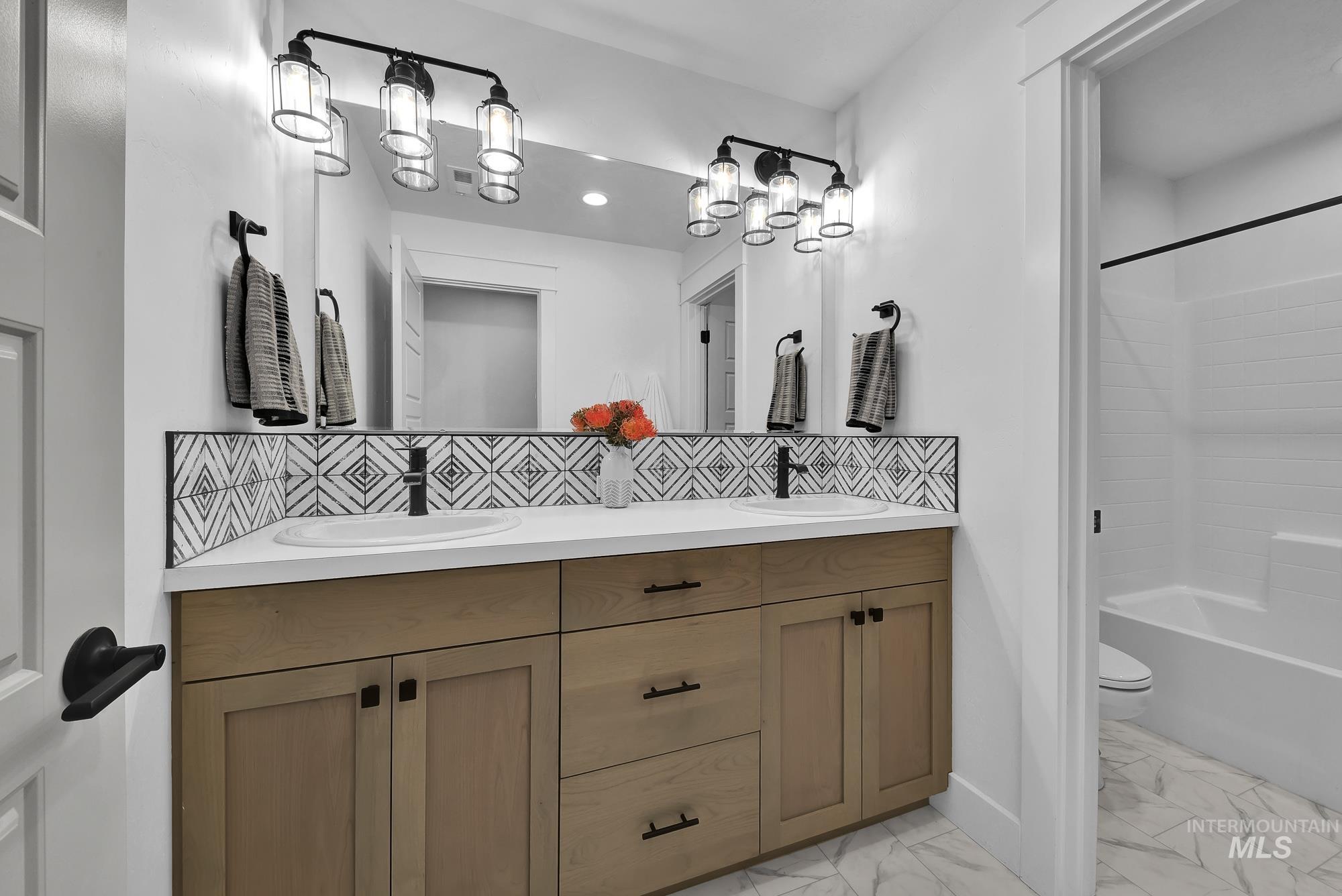 Full bath with backsplash, double vanity, shower / bath combination, and light marble finish floors