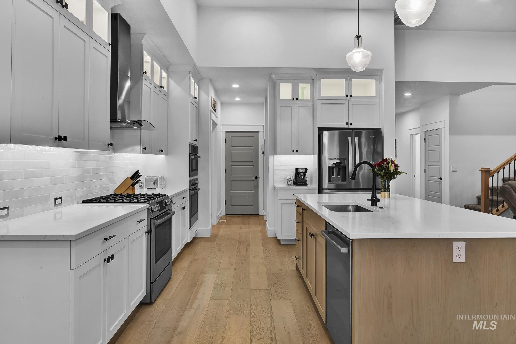 Kitchen featuring stainless steel appliances, hanging light fixtures, light stone countertops, light wood-type flooring, and tasteful backsplash