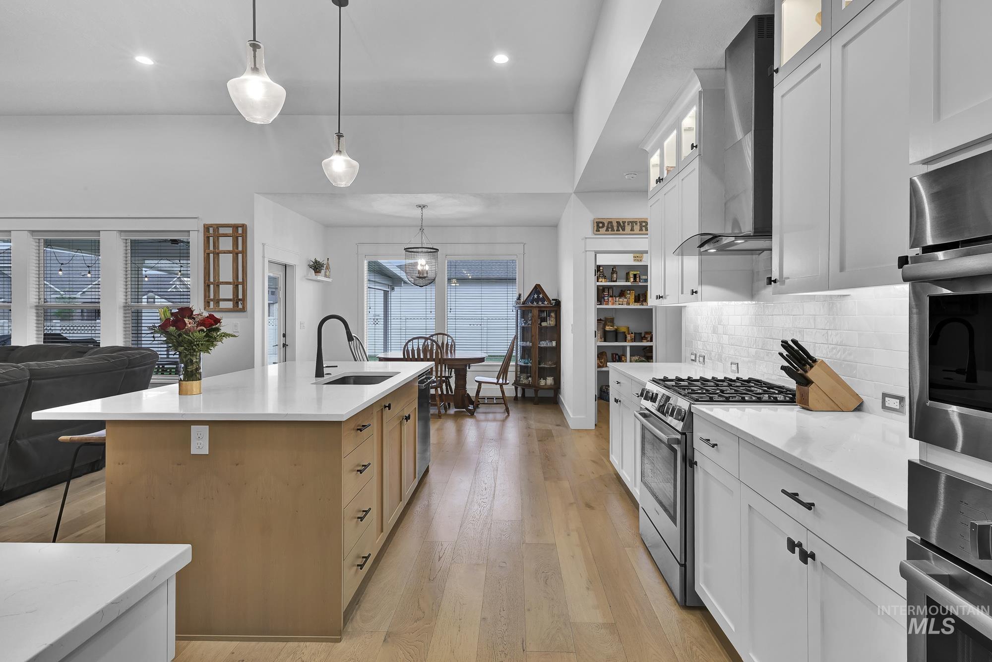 Kitchen with white cabinets, decorative light fixtures, appliances with stainless steel finishes, open floor plan, and wall chimney range hood