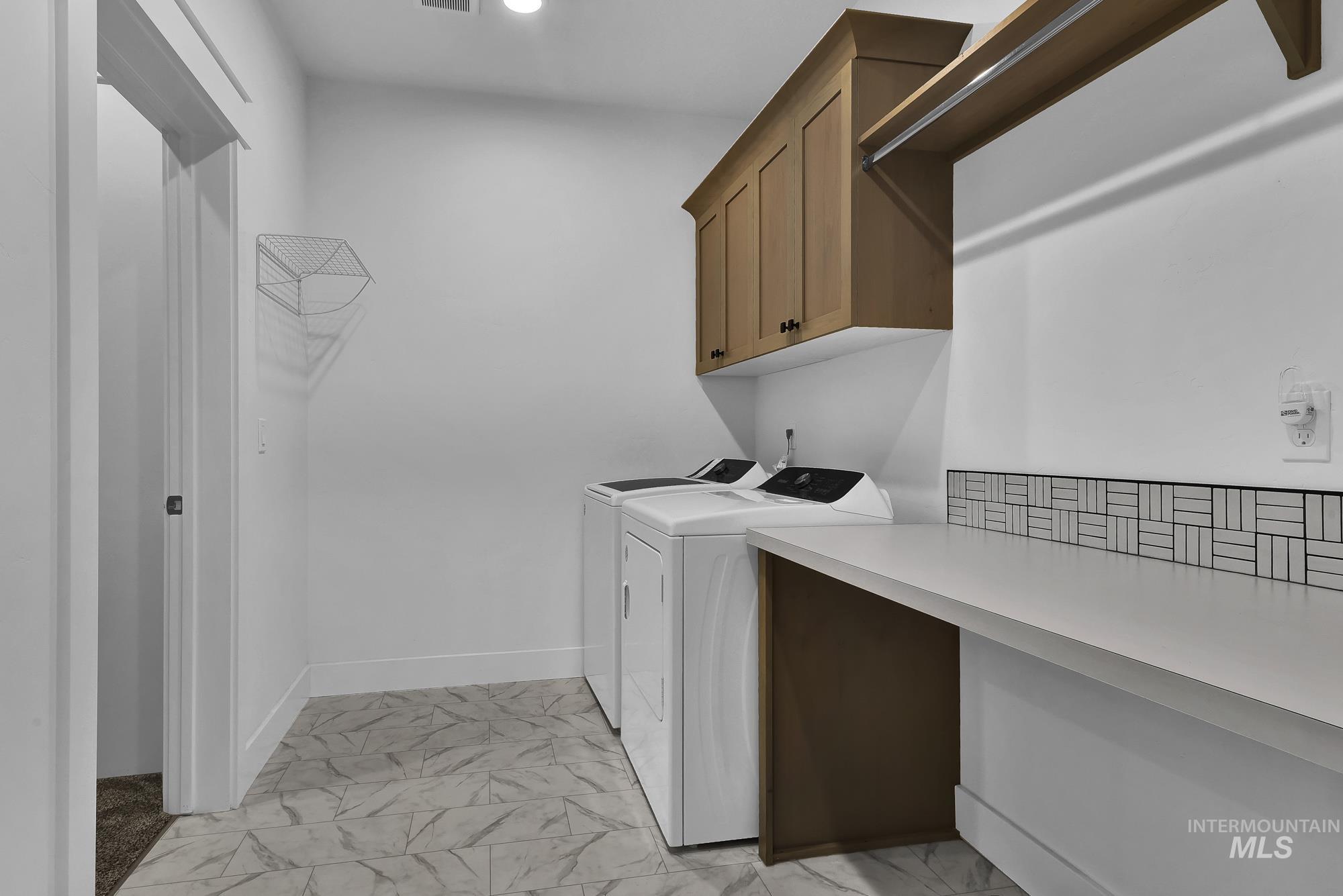 Laundry area with light marble finish flooring, washing machine and dryer, and cabinet space