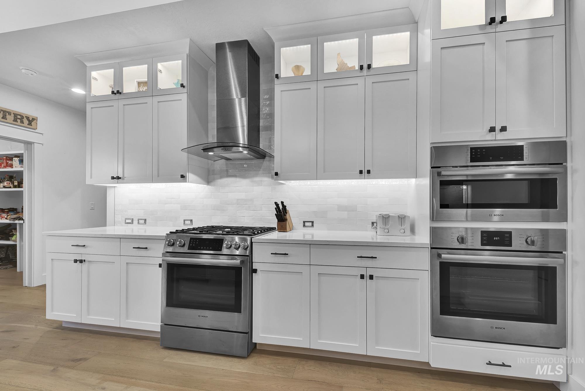 Kitchen with stainless steel appliances, wall chimney exhaust hood, and white cabinetry