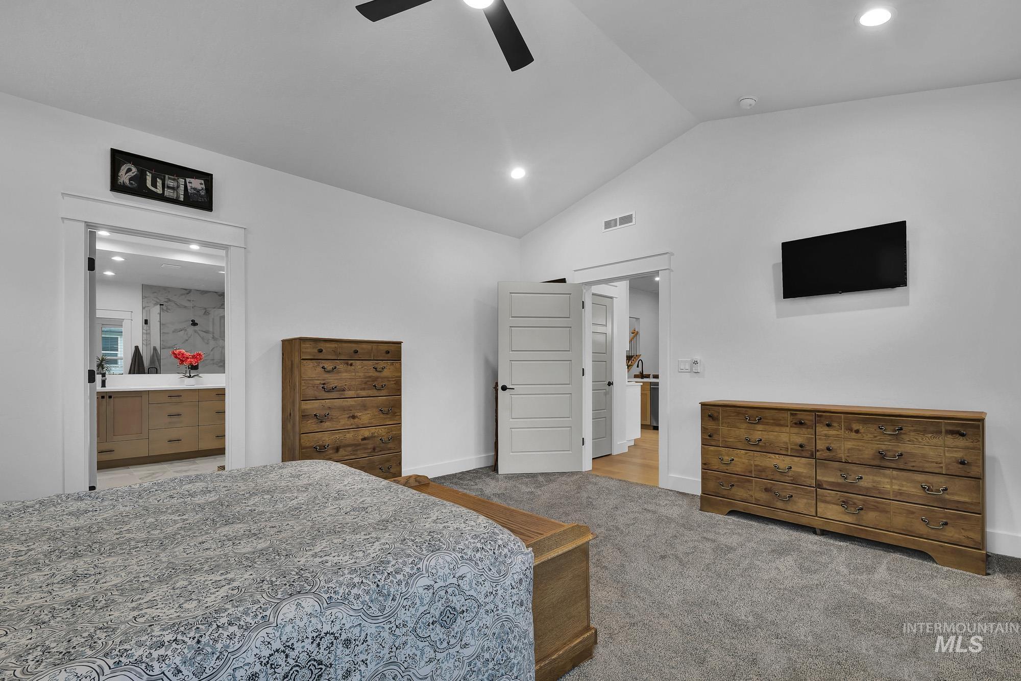 Bedroom with vaulted ceiling, light carpet, ceiling fan, recessed lighting, and ensuite bath