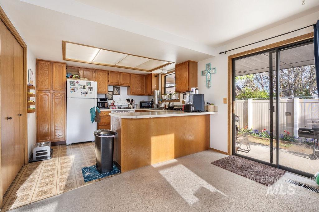 Kitchen featuring wood finish cabinetry, a peninsula, freestanding refrigerator, light countertops, and light floors