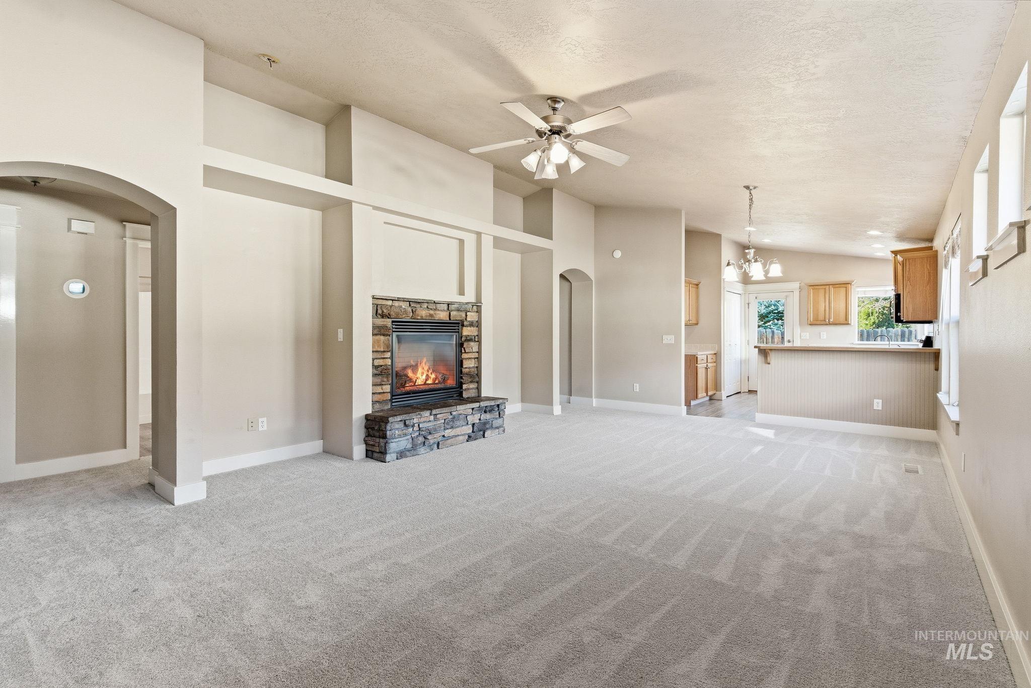 Unfurnished living room with arched walkways, lofted ceiling, a stone fireplace, a ceiling fan, and light colored carpet