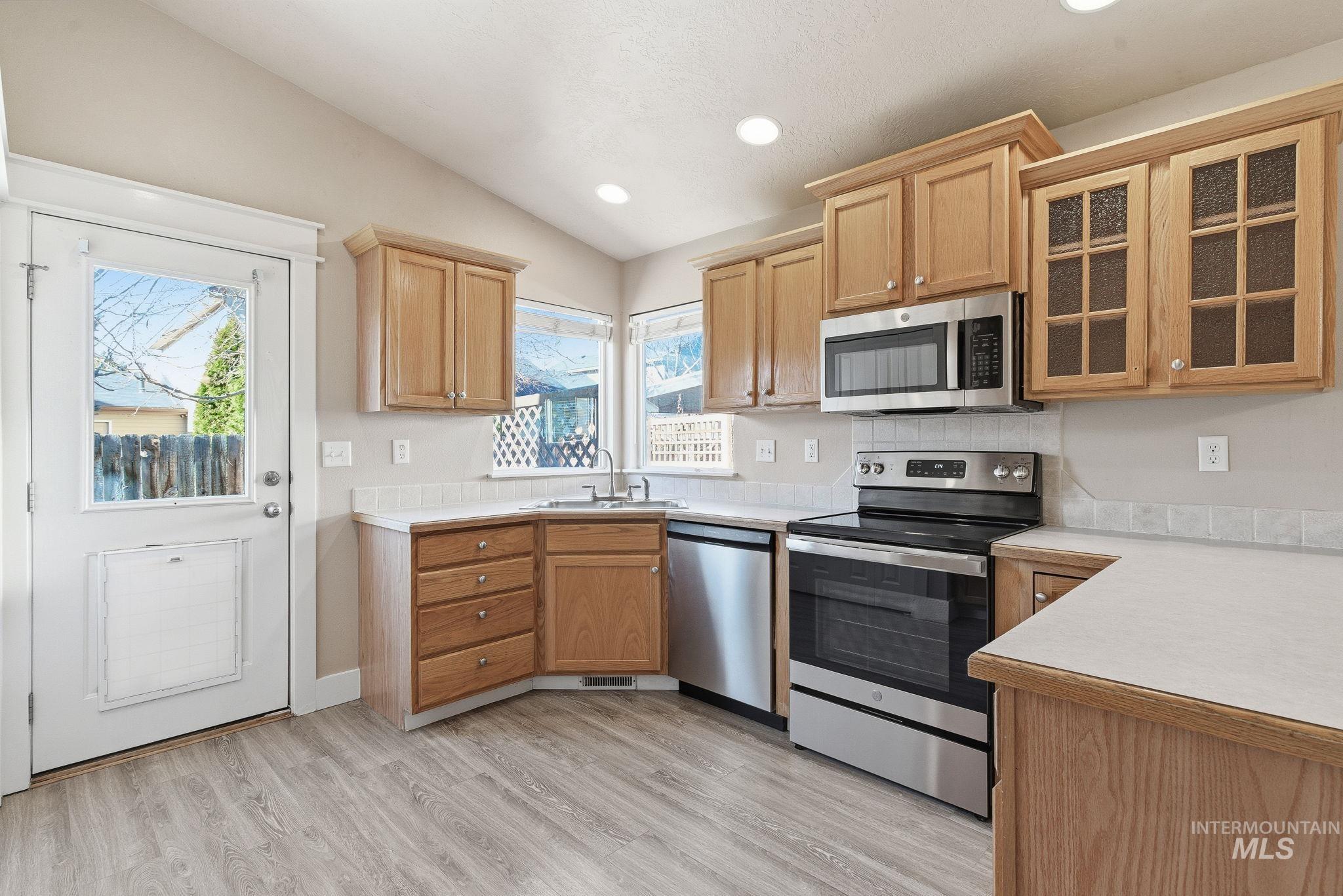 Kitchen featuring appliances with stainless steel finishes, light countertops, lofted ceiling, glass insert cabinets, and recessed lighting