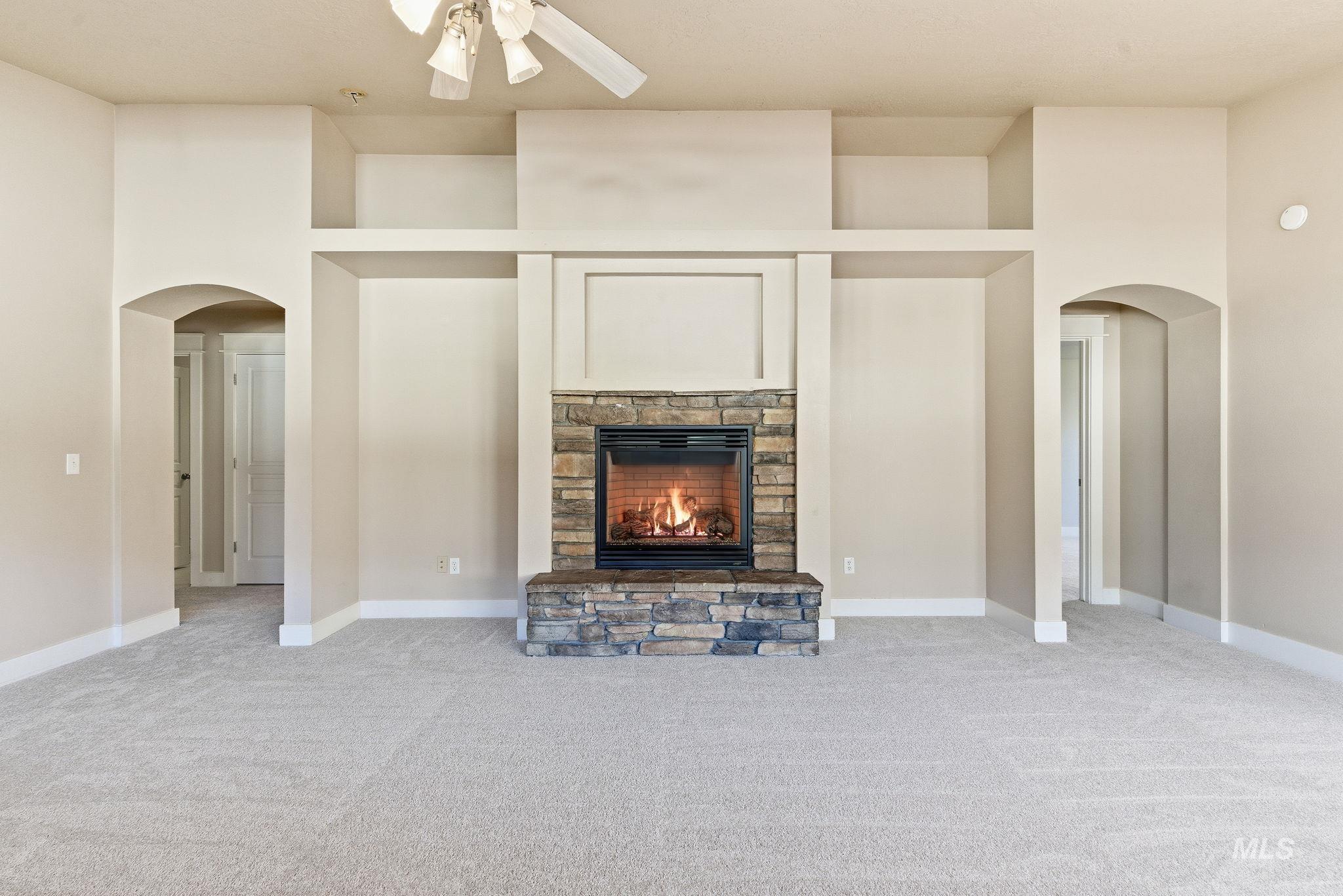 Unfurnished living room with arched walkways, a fireplace, light colored carpet, and ceiling fan