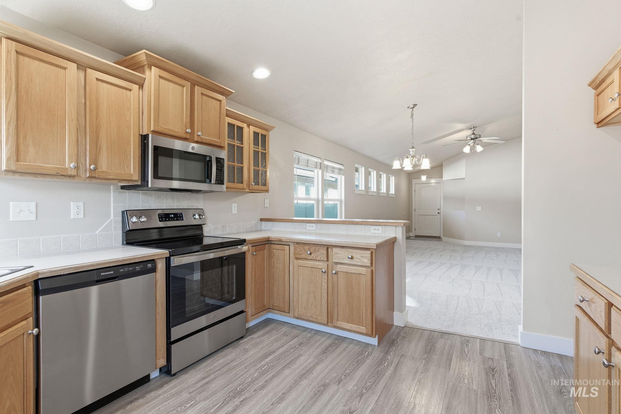 Kitchen featuring appliances with stainless steel finishes, a peninsula, light countertops, glass insert cabinets, and vaulted ceiling