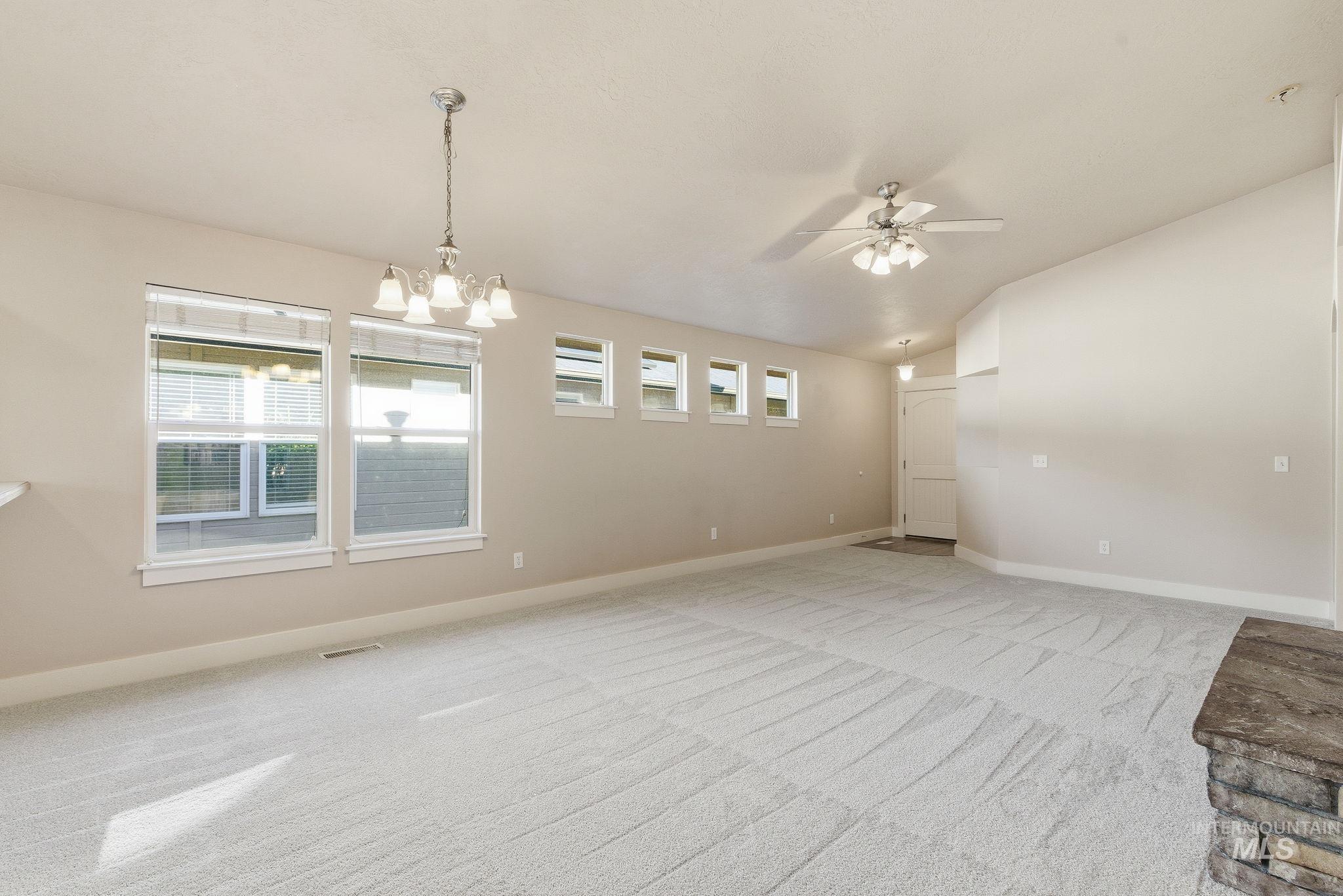 Unfurnished room with plenty of natural light, light colored carpet, a ceiling fan, lofted ceiling, and a chandelier