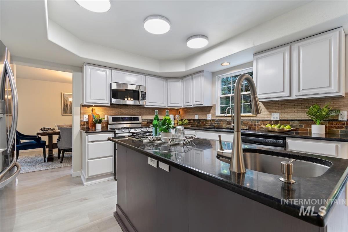 Kitchen featuring appliances with stainless steel finishes, white cabinetry, dark stone counters, and tasteful backsplash