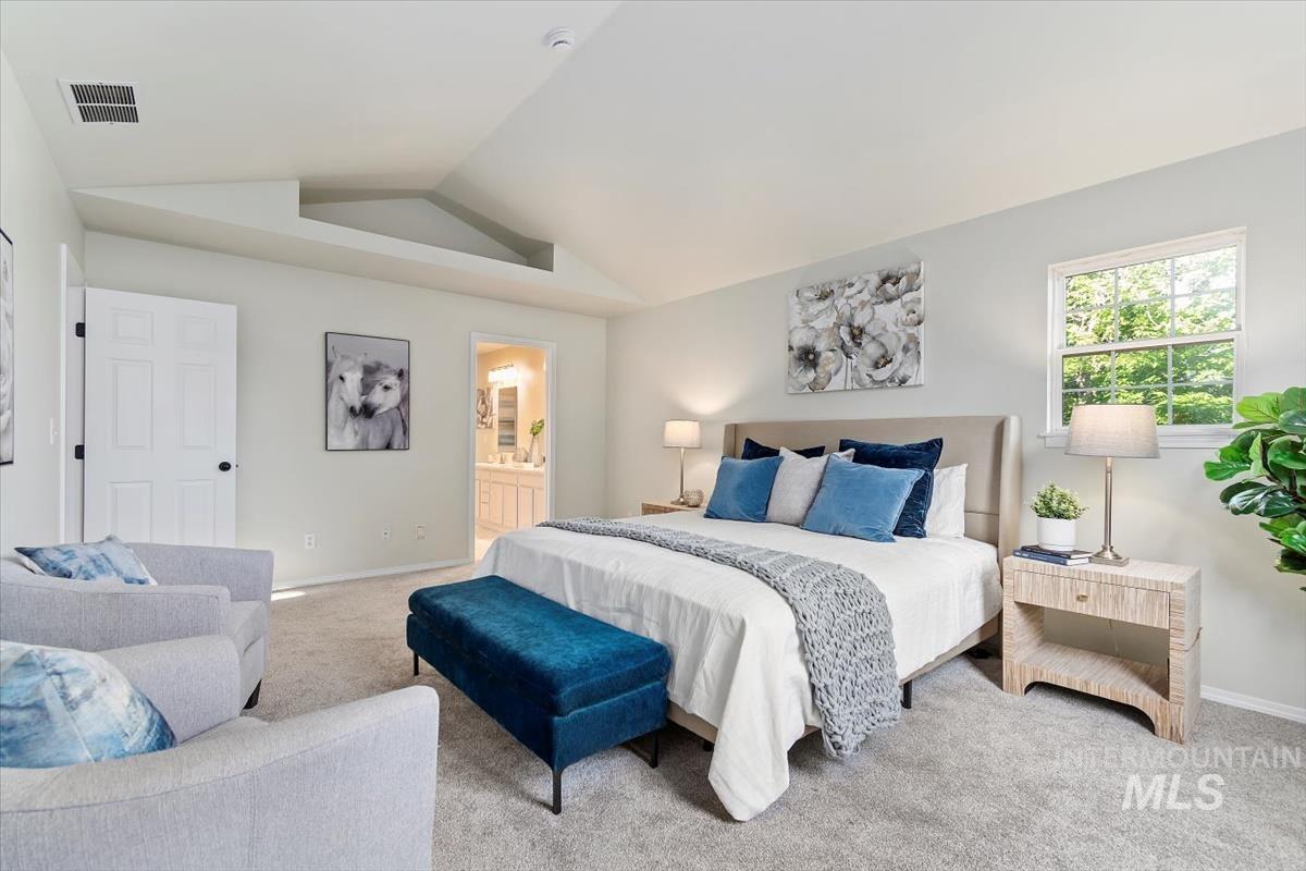 Bedroom with light colored carpet, lofted ceiling, and ensuite bathroom