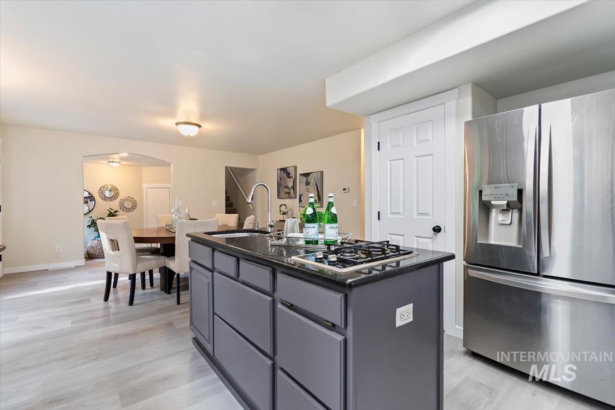 Kitchen with stainless steel fridge, gas cooktop, gray cabinetry, an island with sink, and arched walkways