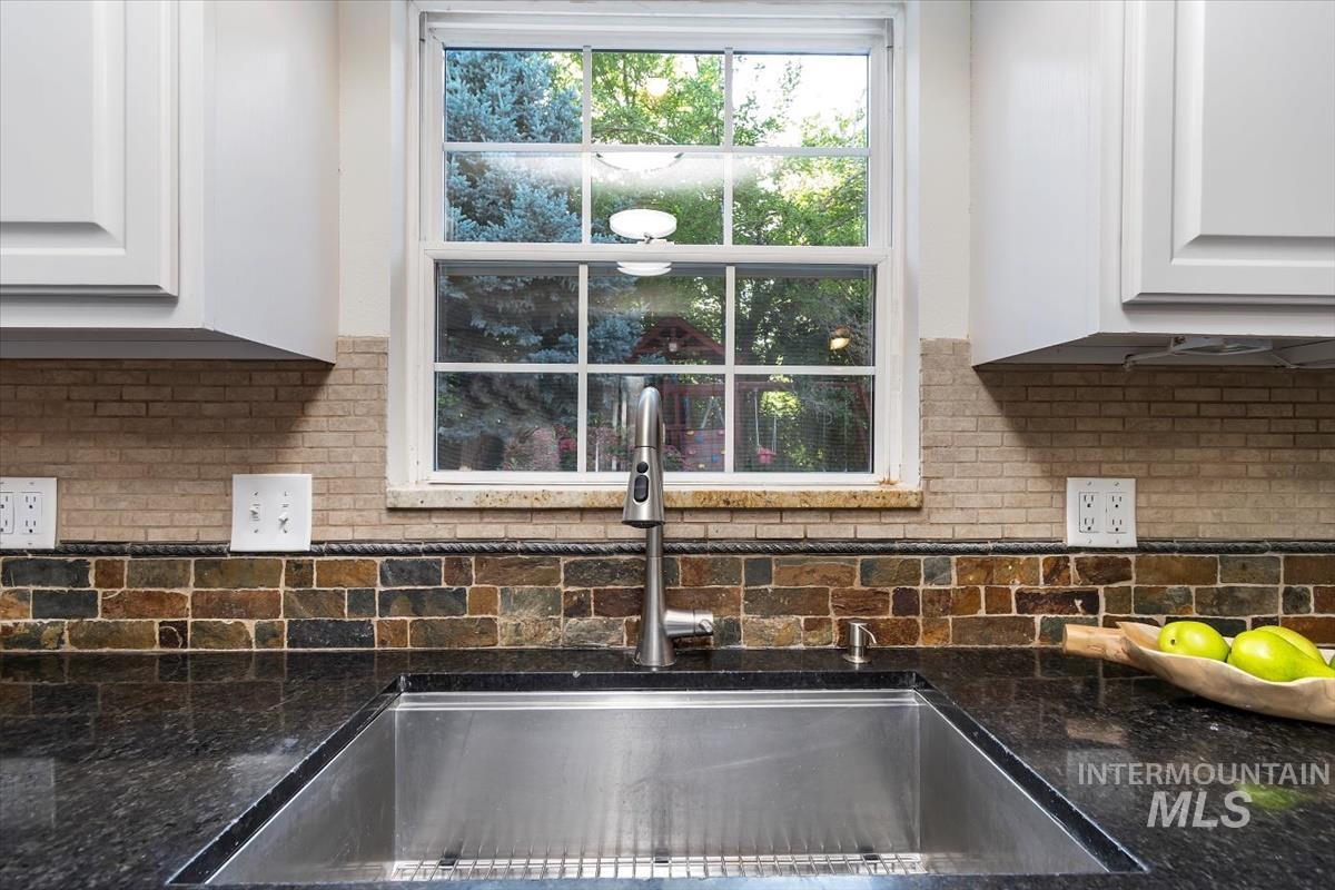 Kitchen view of decorative backsplash, white cabinets, and dark stone countertops