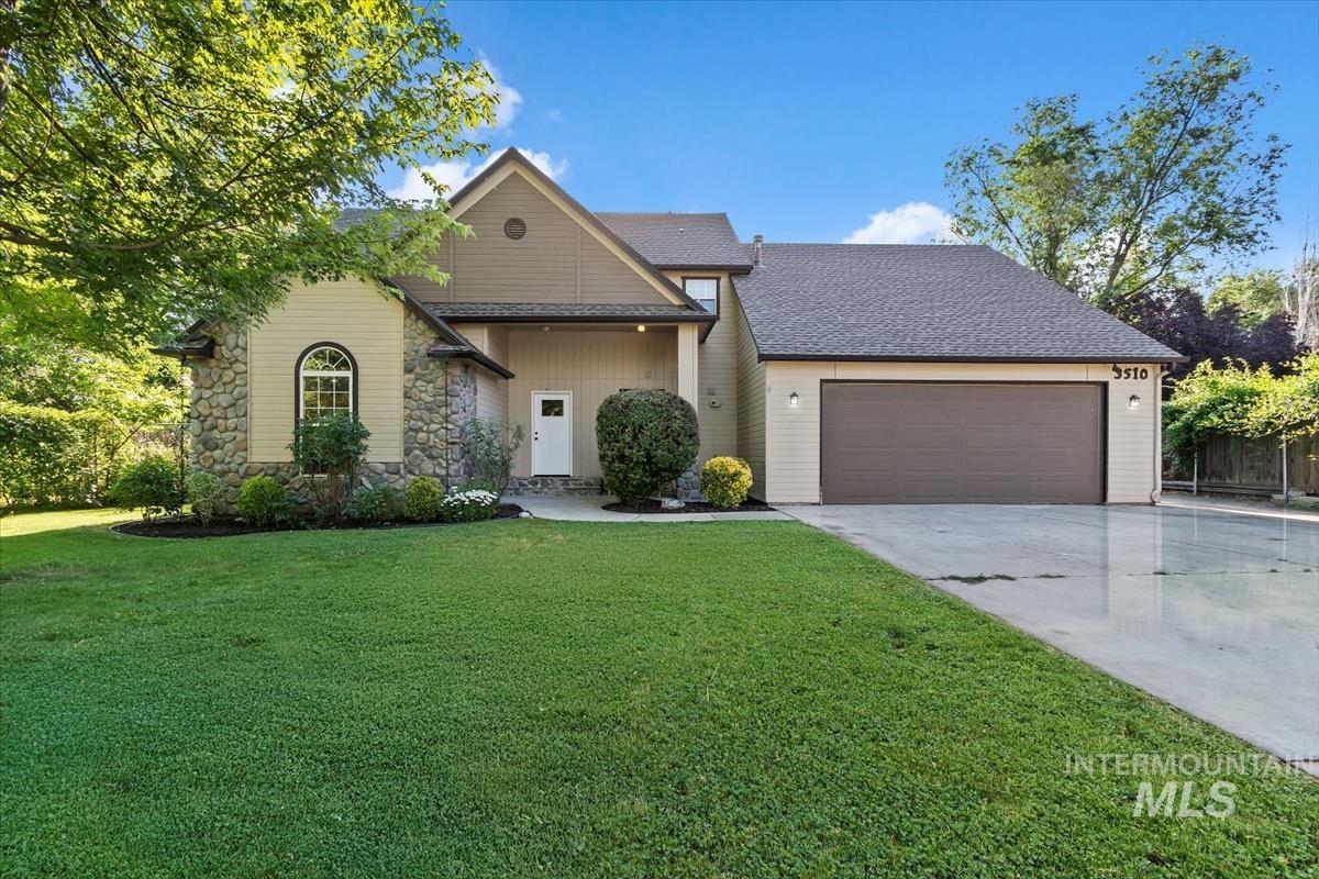 View of front of property featuring concrete driveway, an attached garage, a front yard, stone siding, and a shingled roof