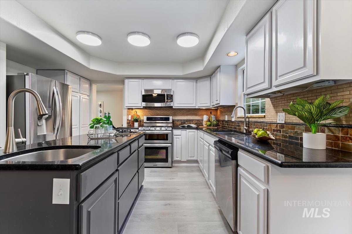Kitchen featuring appliances with stainless steel finishes, white cabinets, decorative backsplash, and a kitchen island with sink