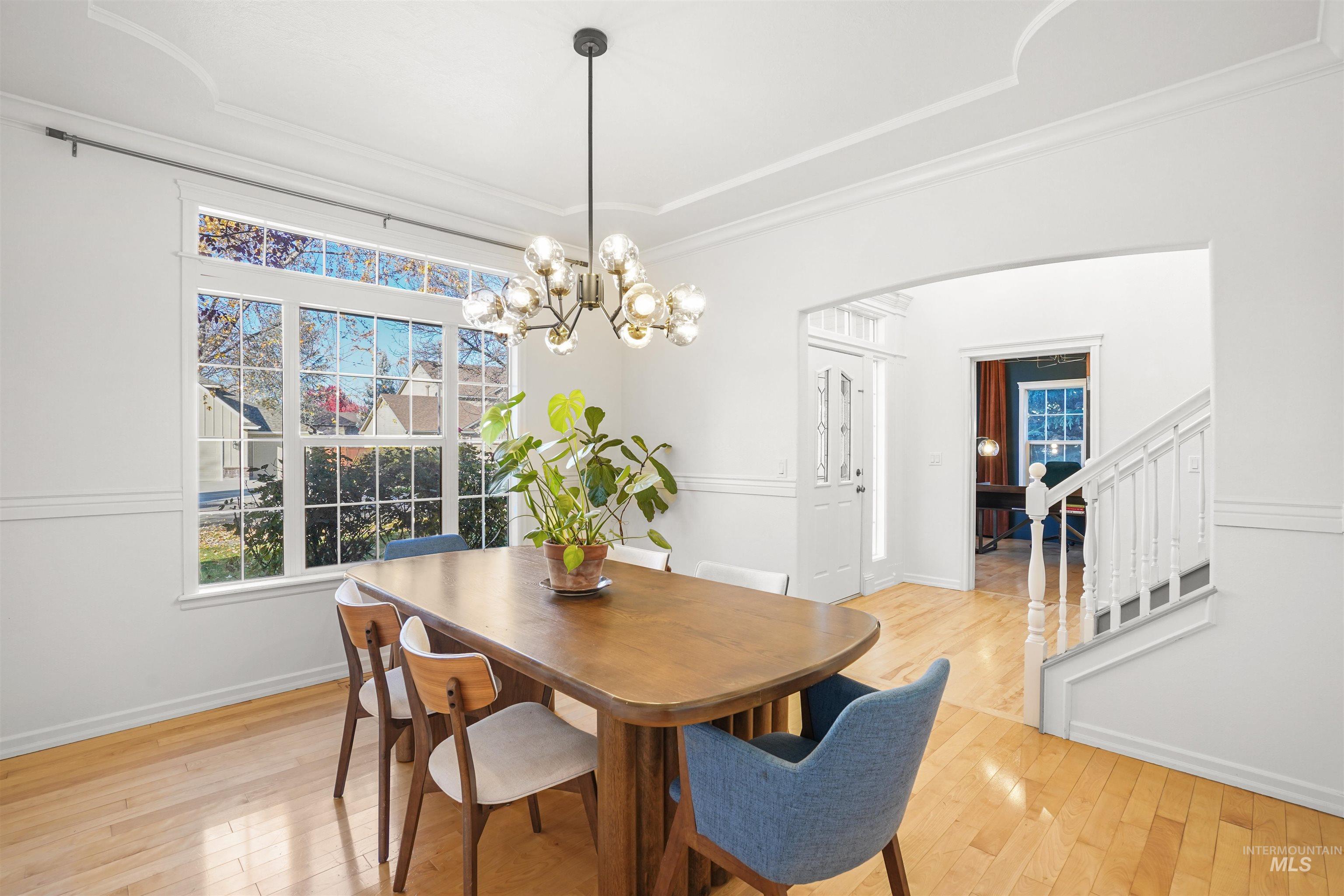 Dining area with light wood-type flooring, stairs, crown molding, arched walkways, and a chandelier
