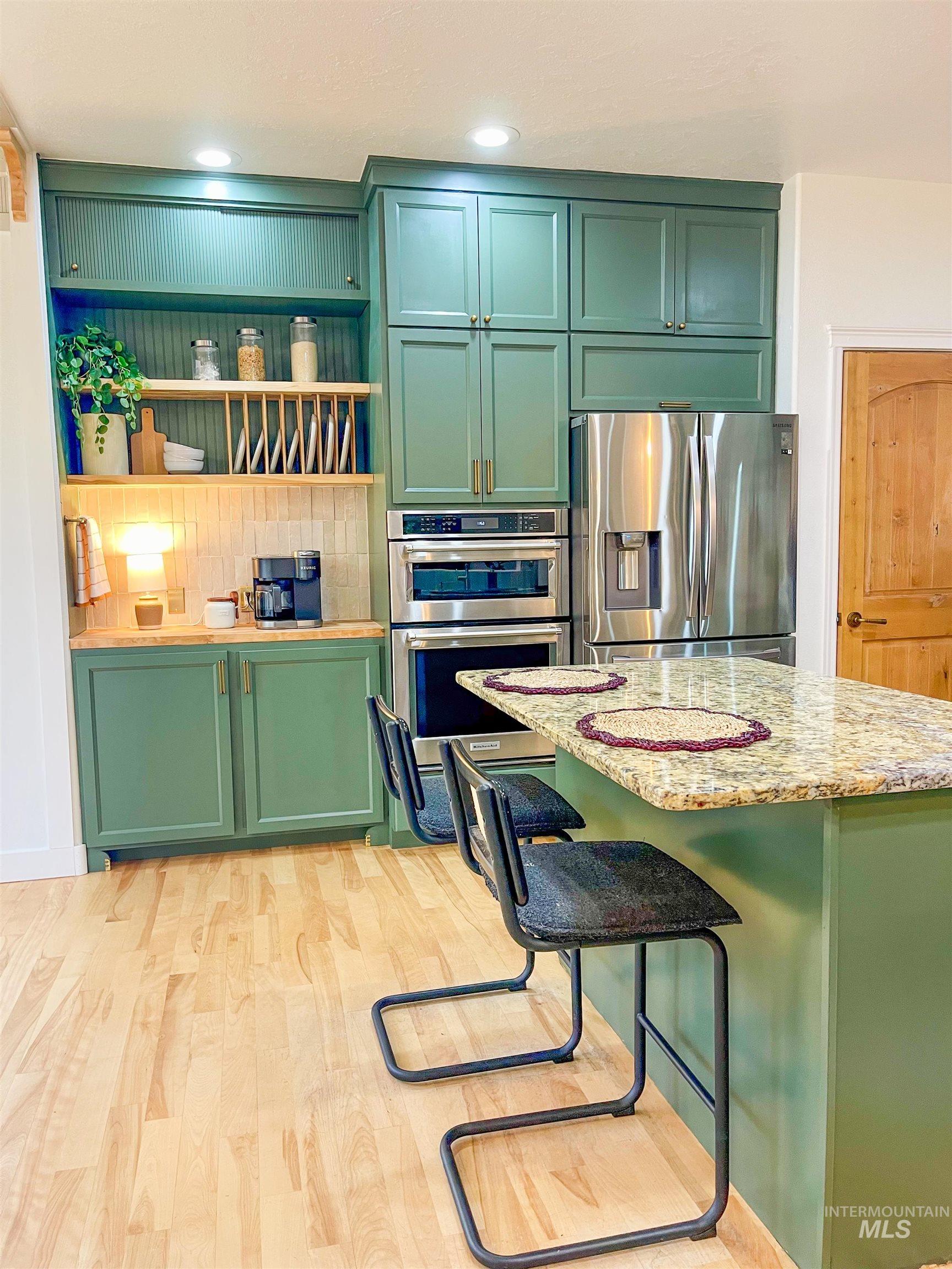 Kitchen with green cabinets, stainless steel appliances, light wood-style floors, a breakfast bar, and light stone counters
