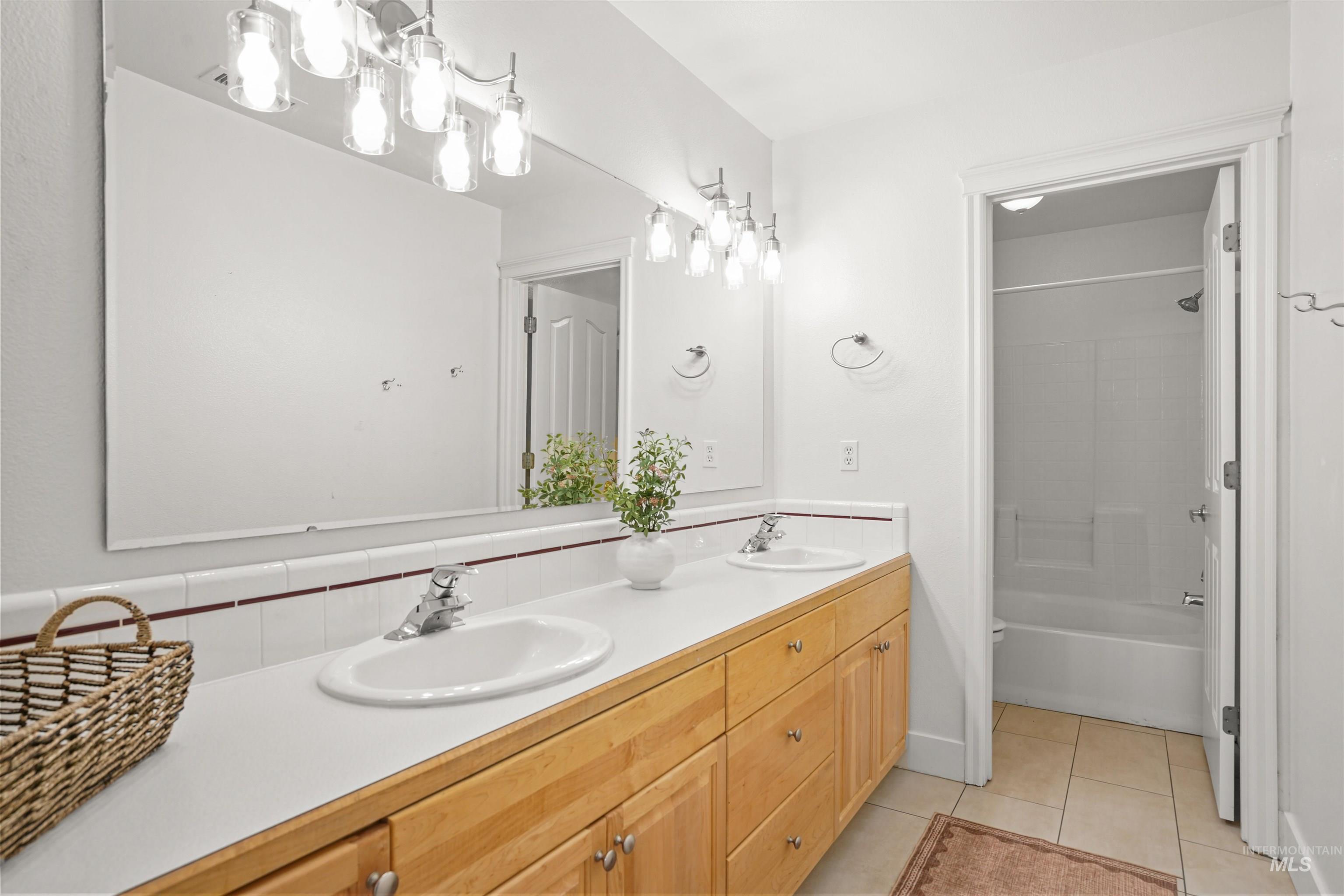 Full bathroom with double vanity, light tile patterned floors, bathtub / shower combination, and decorative backsplash