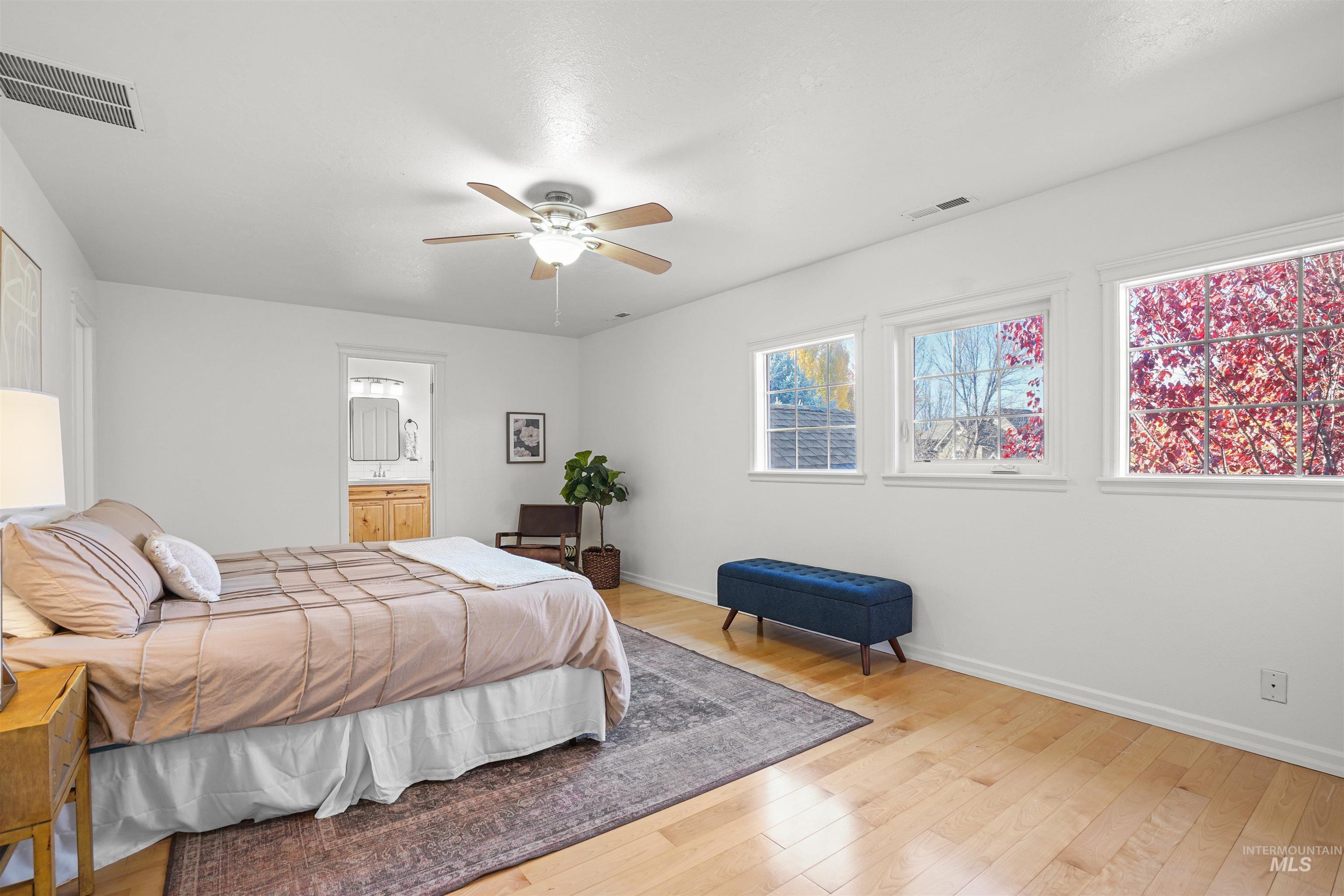 Bedroom with light wood-style floors, a ceiling fan, and connected bathroom