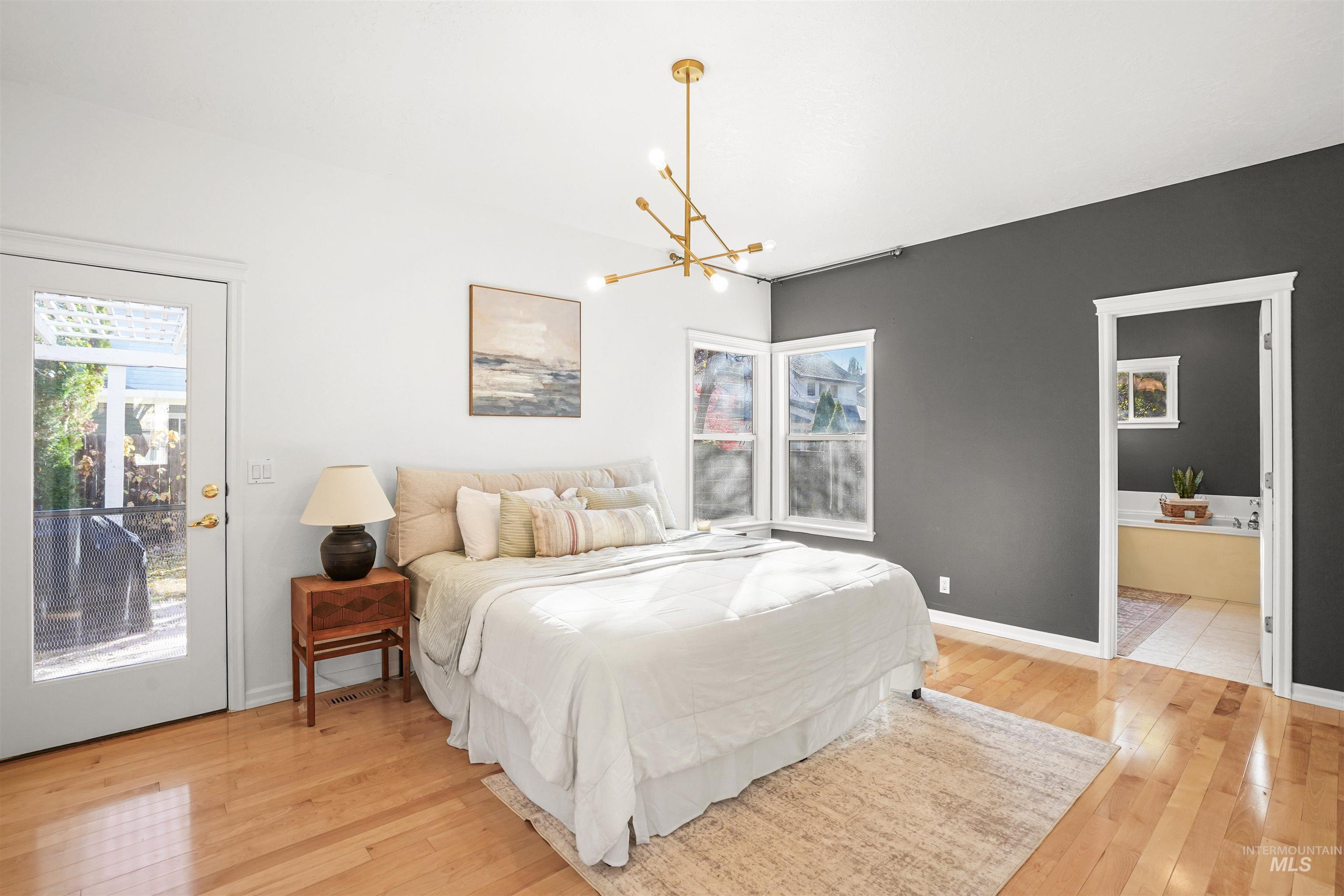 Bedroom with access to exterior, light wood-style floors, a chandelier, and ensuite bathroom