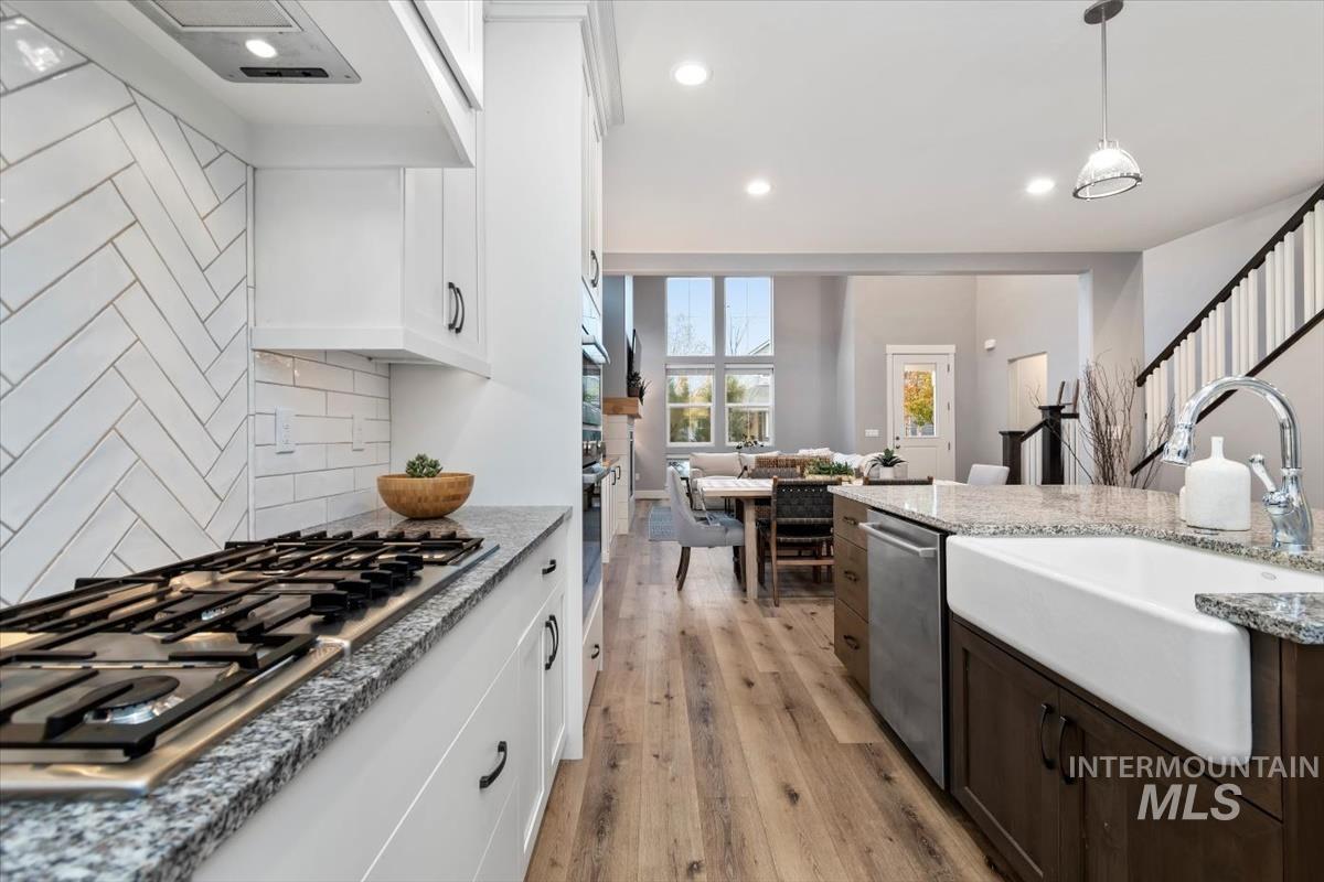 Kitchen with hanging light fixtures, light wood-type flooring, stainless steel appliances, white cabinets, and recessed lighting